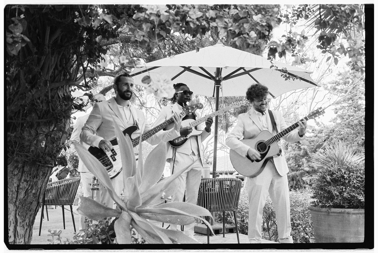 Musicians in white suits performing with instruments at an outdoor event.
