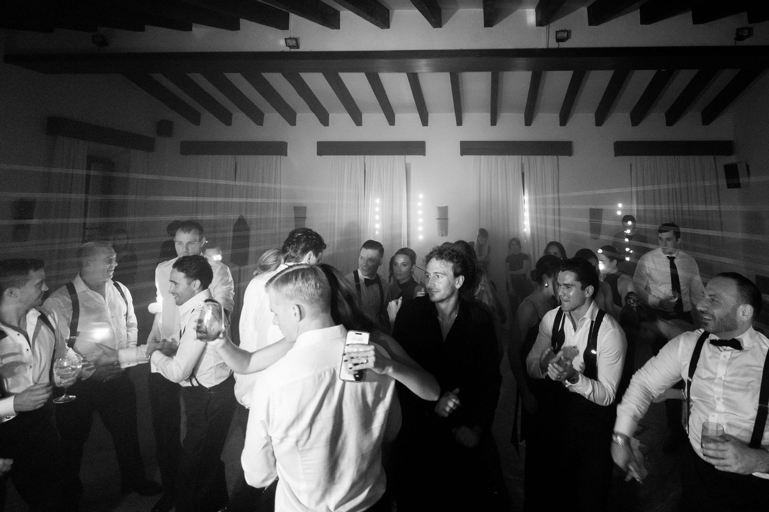 Wedding guests dancing and celebrating on a dark dance floor with dramatic overhead lighting.