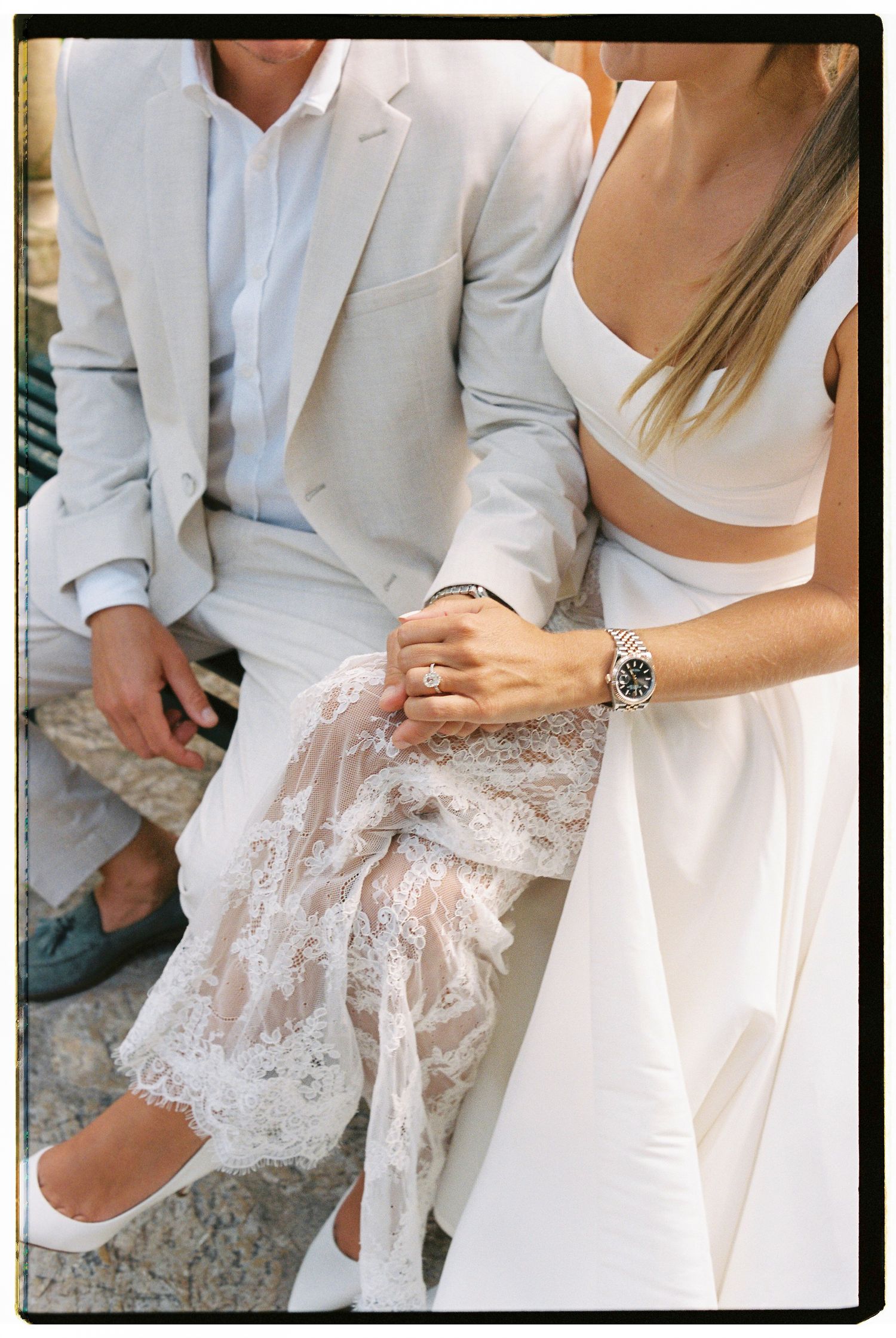 Close-up details of white lace and fabric being held by people wearing white formal attire.