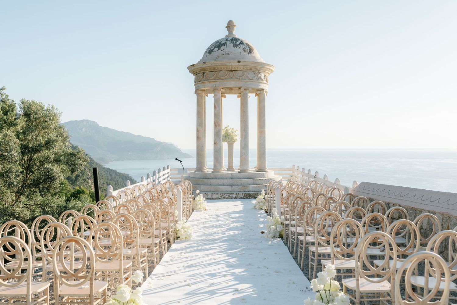 Classical white stone gazebo with ornate columns set against a blue sky.