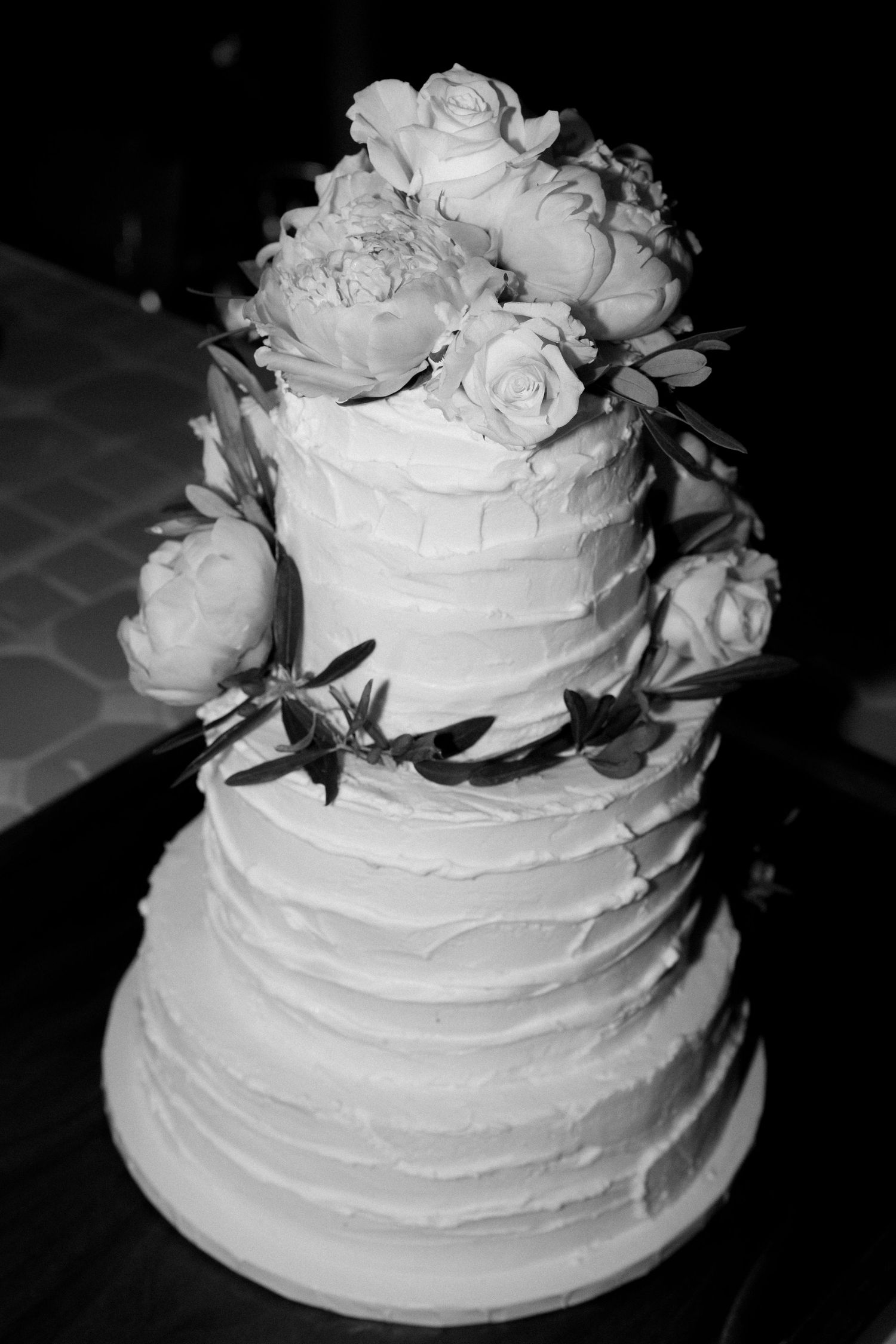 Elegant white tiered wedding cake decorated with fresh roses and buttercream frosting.