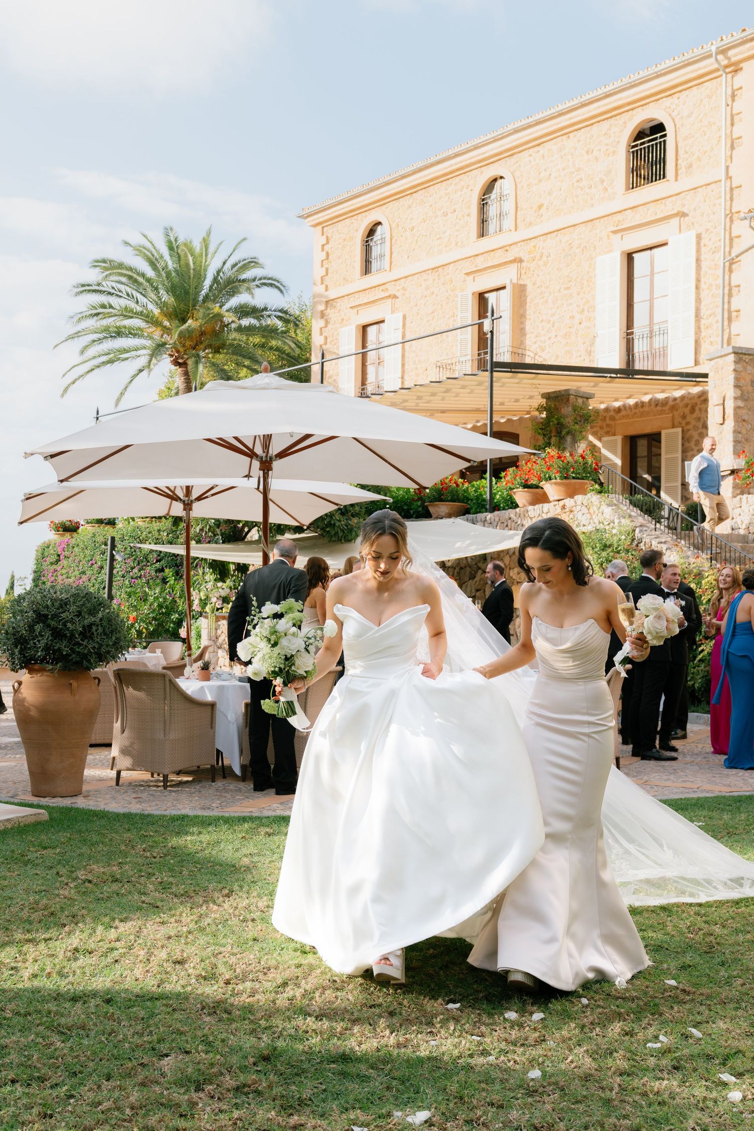 Bridesmaids in white dresses twirl and dance under garden umbrellas at elegant outdoor venue.