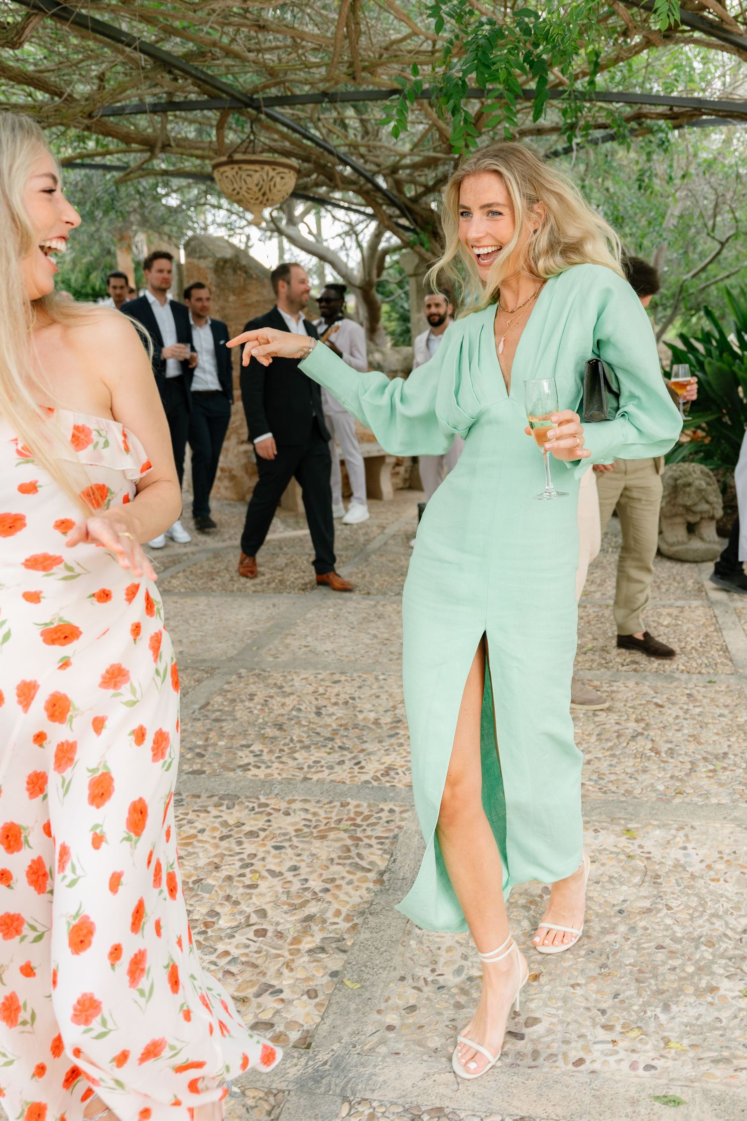 Wedding guests dancing on a stone patio in colorful summer dresses.