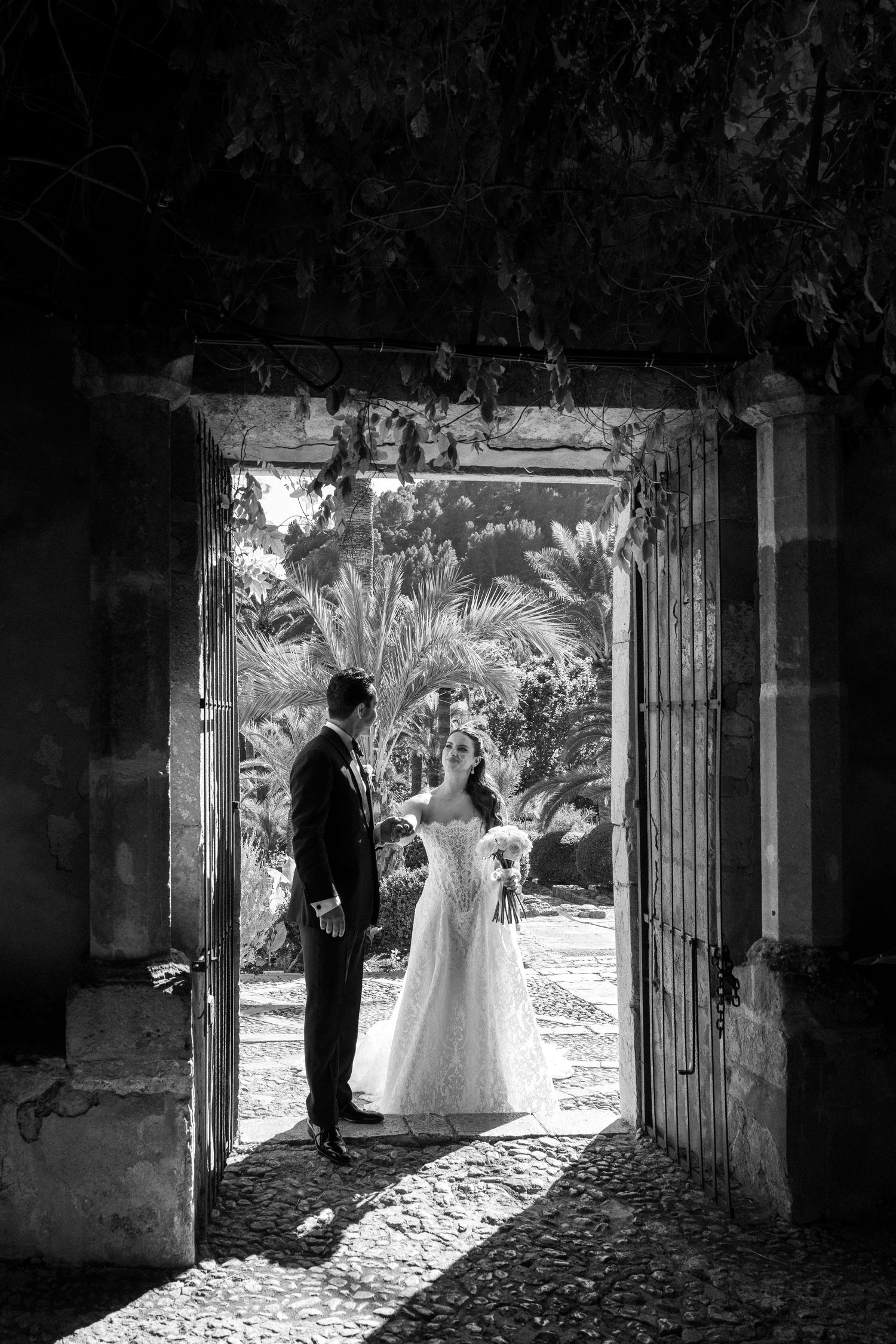 Black and white wedding photo of bride and groom standing in an ornate doorway with palm trees in background.