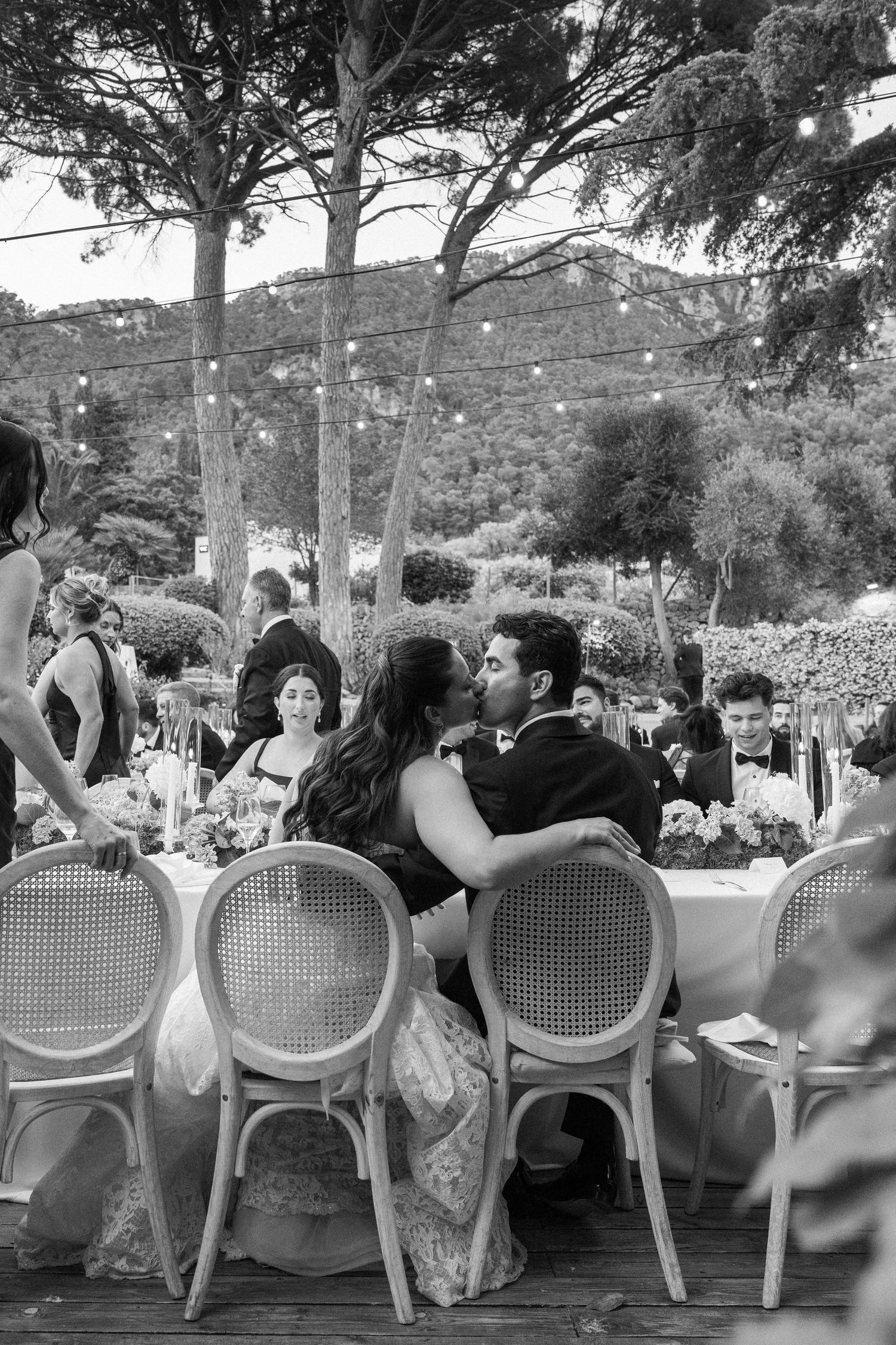 Black and white photo of a couple sharing a romantic moment at an outdoor wedding reception dinner table.