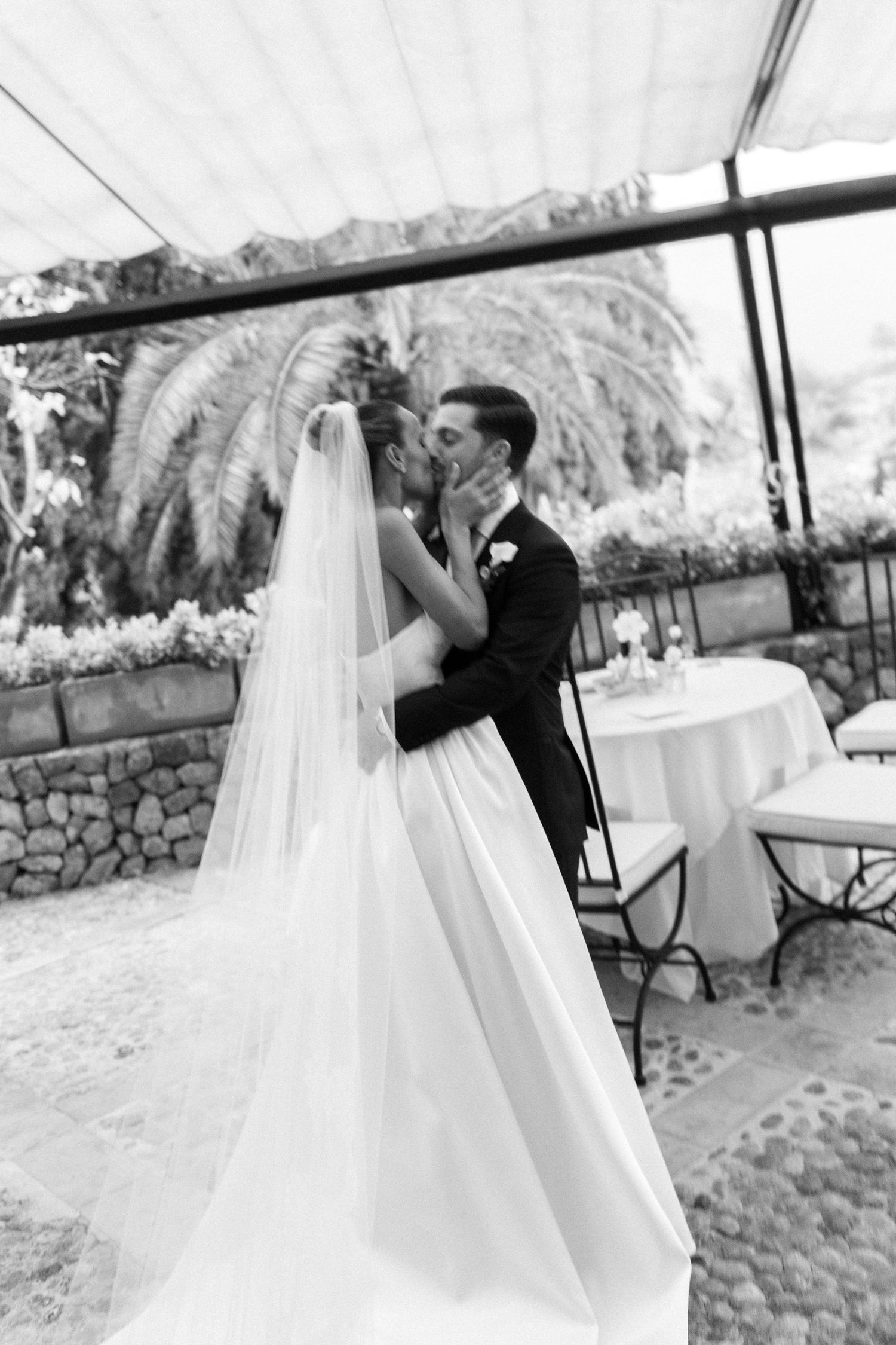 Black and white photo of flowing wedding dress captured in elegant greenhouse setting.