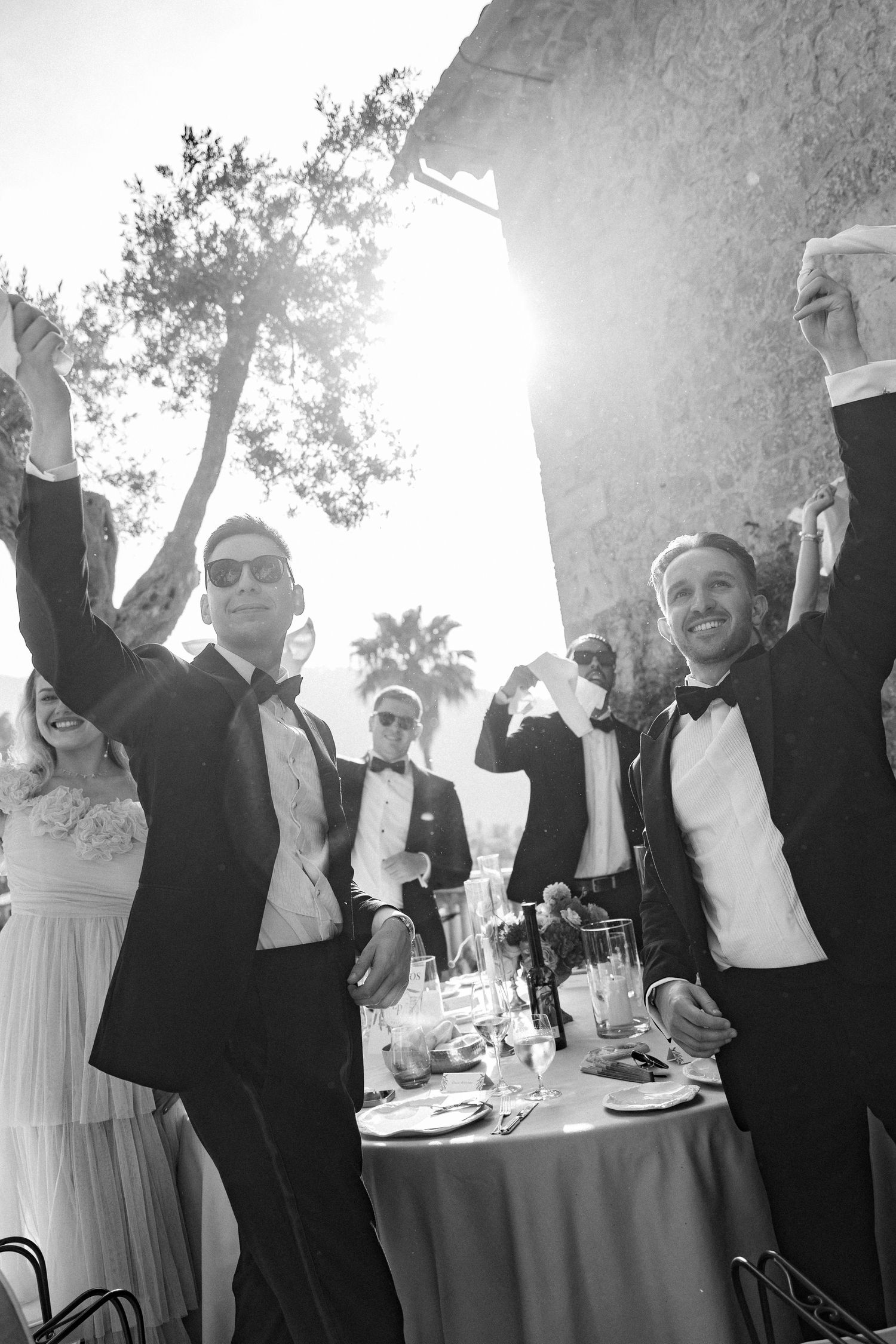 Wedding party celebrating with raised arms in black and white formal attire.