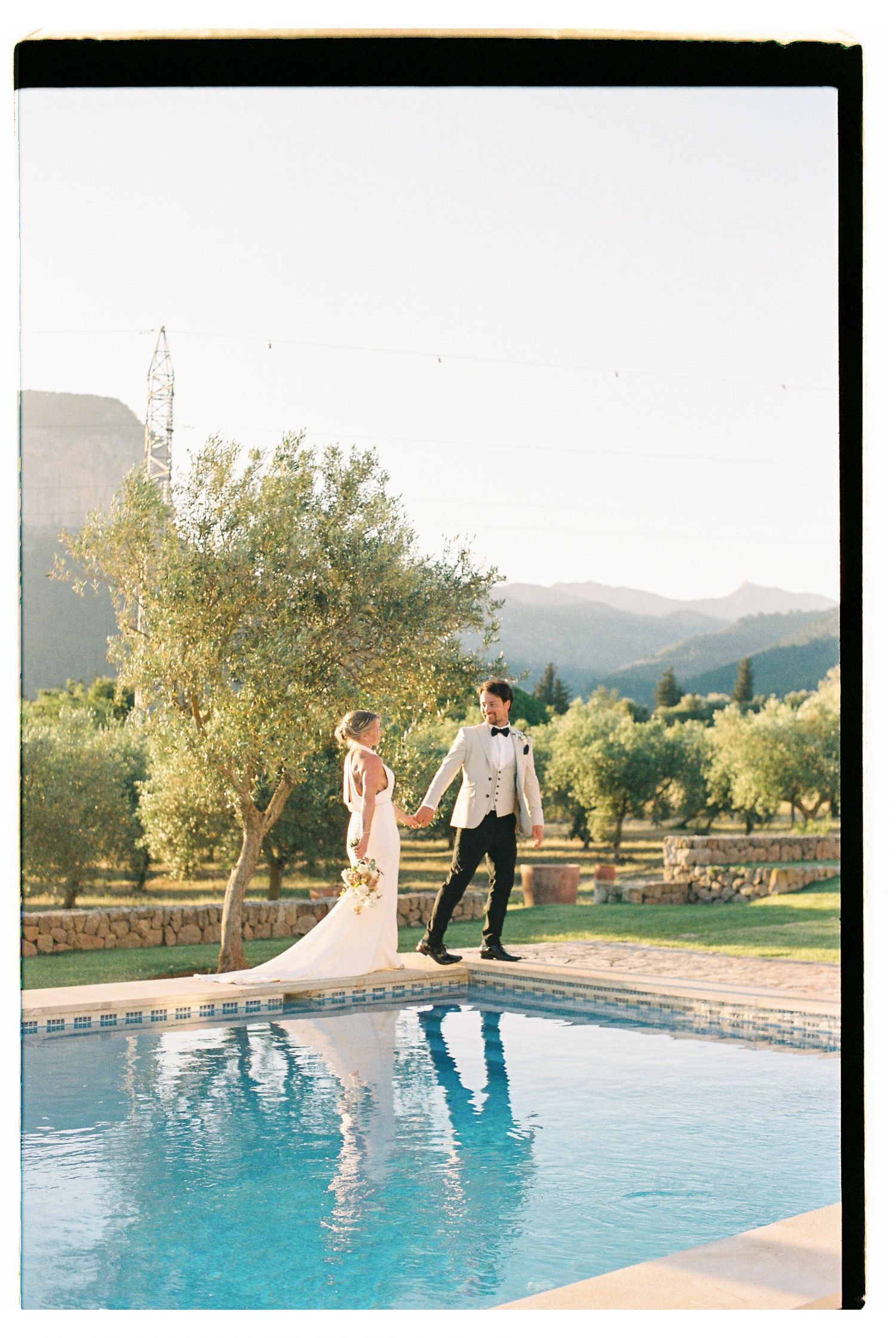 A couple posing by a swimming pool with mountains in the background.