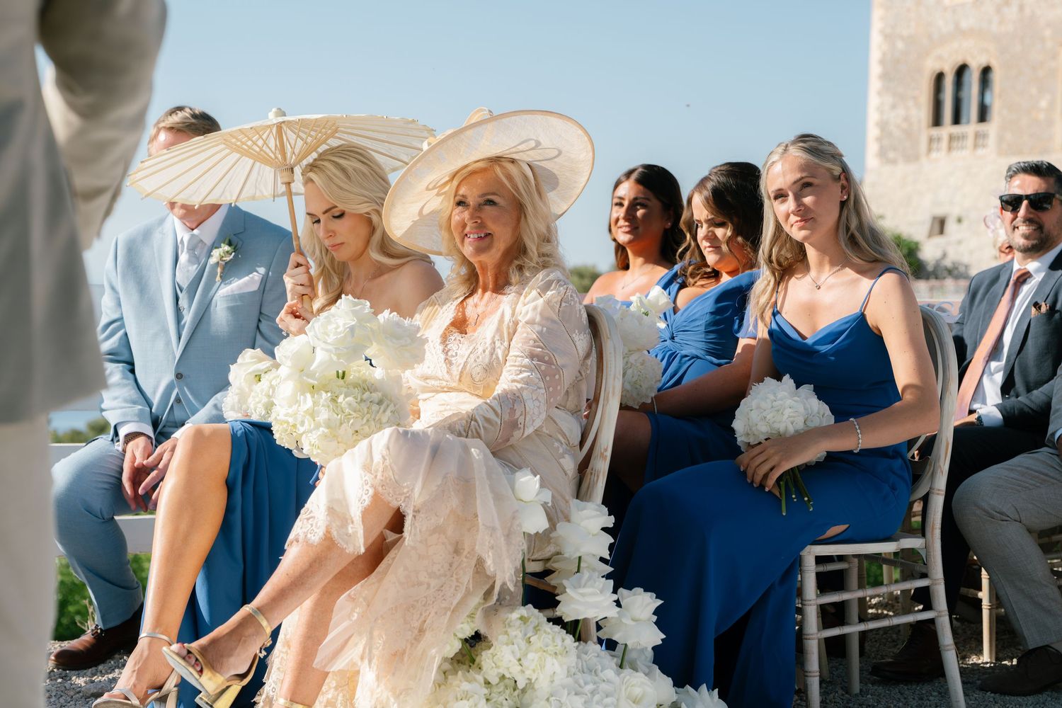 Wedding guests holding white parasols during outdoor celebration.
