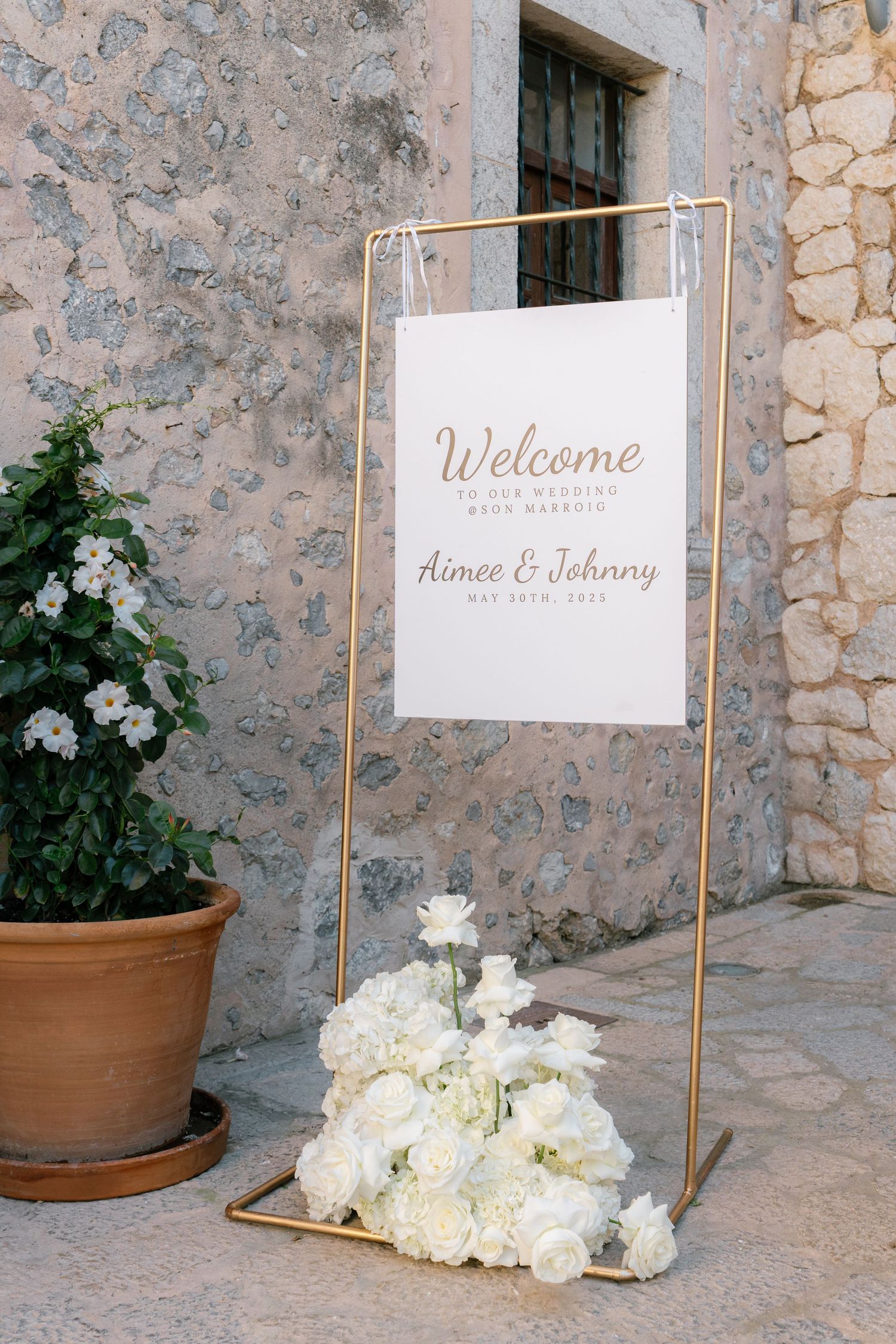 Wedding welcome signs with white flowers displayed against rustic stone walls.