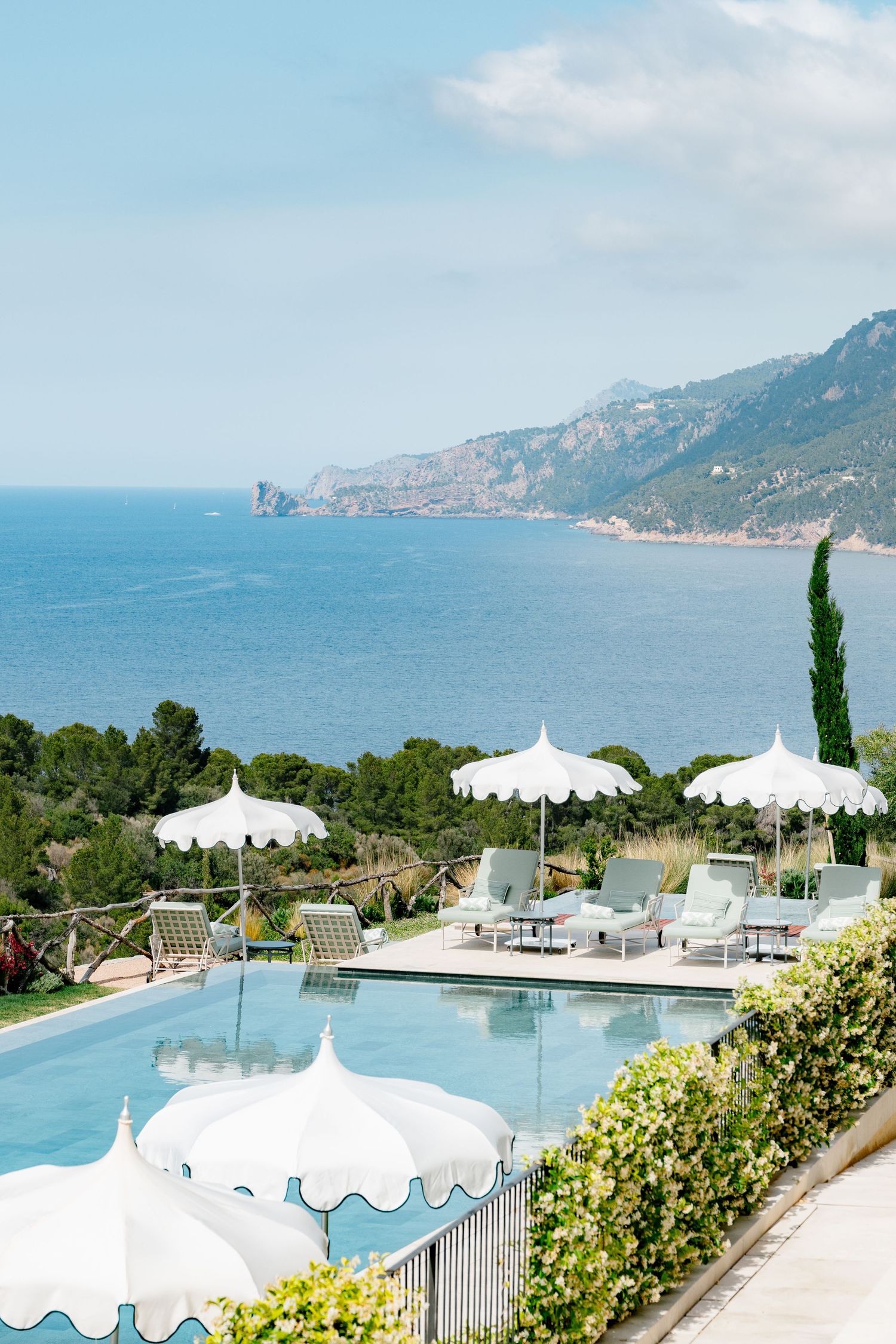 Luxury resort infinity pool with white umbrellas overlooking Mediterranean coastal mountains and sea views.