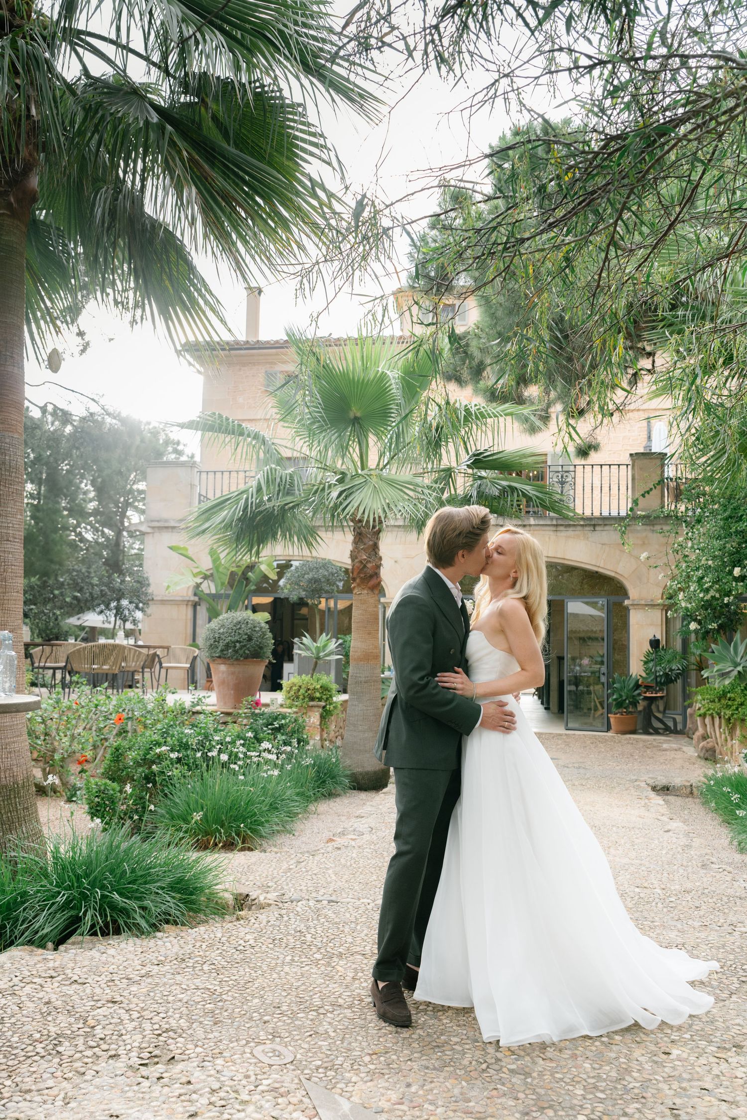 Newlyweds share an intimate moment in a Mediterranean courtyard with palm trees.