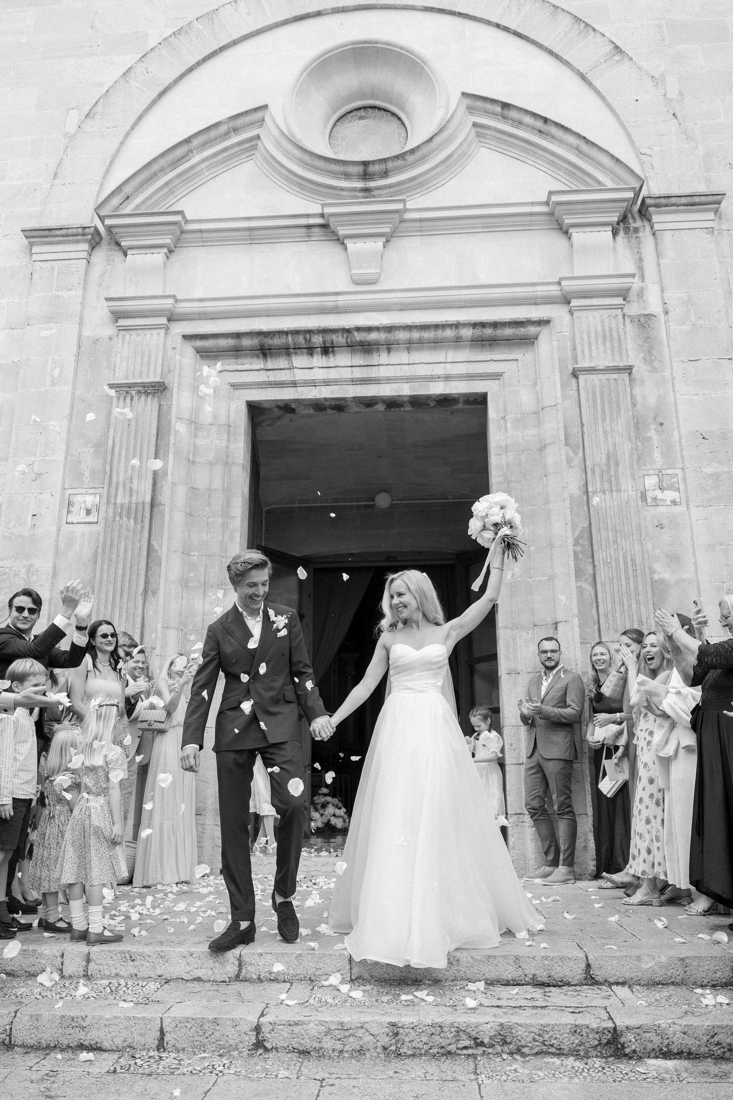 Black and white photo of wedding celebration exit with confetti toss outside church steps.