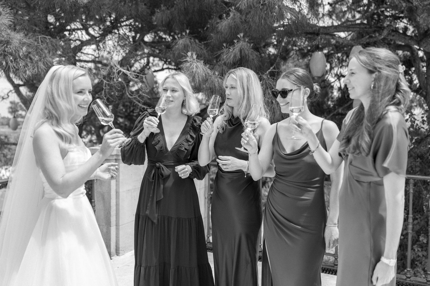 Wedding party in black dresses reacting emotionally outdoors.