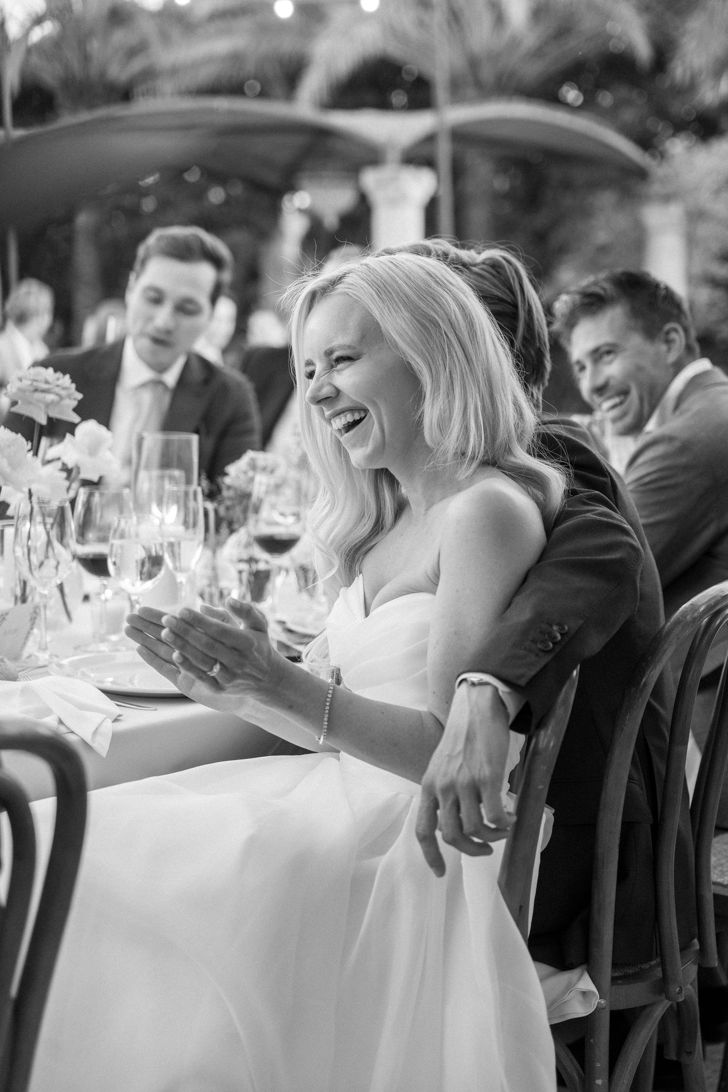 Bride in white dress laughs joyfully during wedding reception dinner.