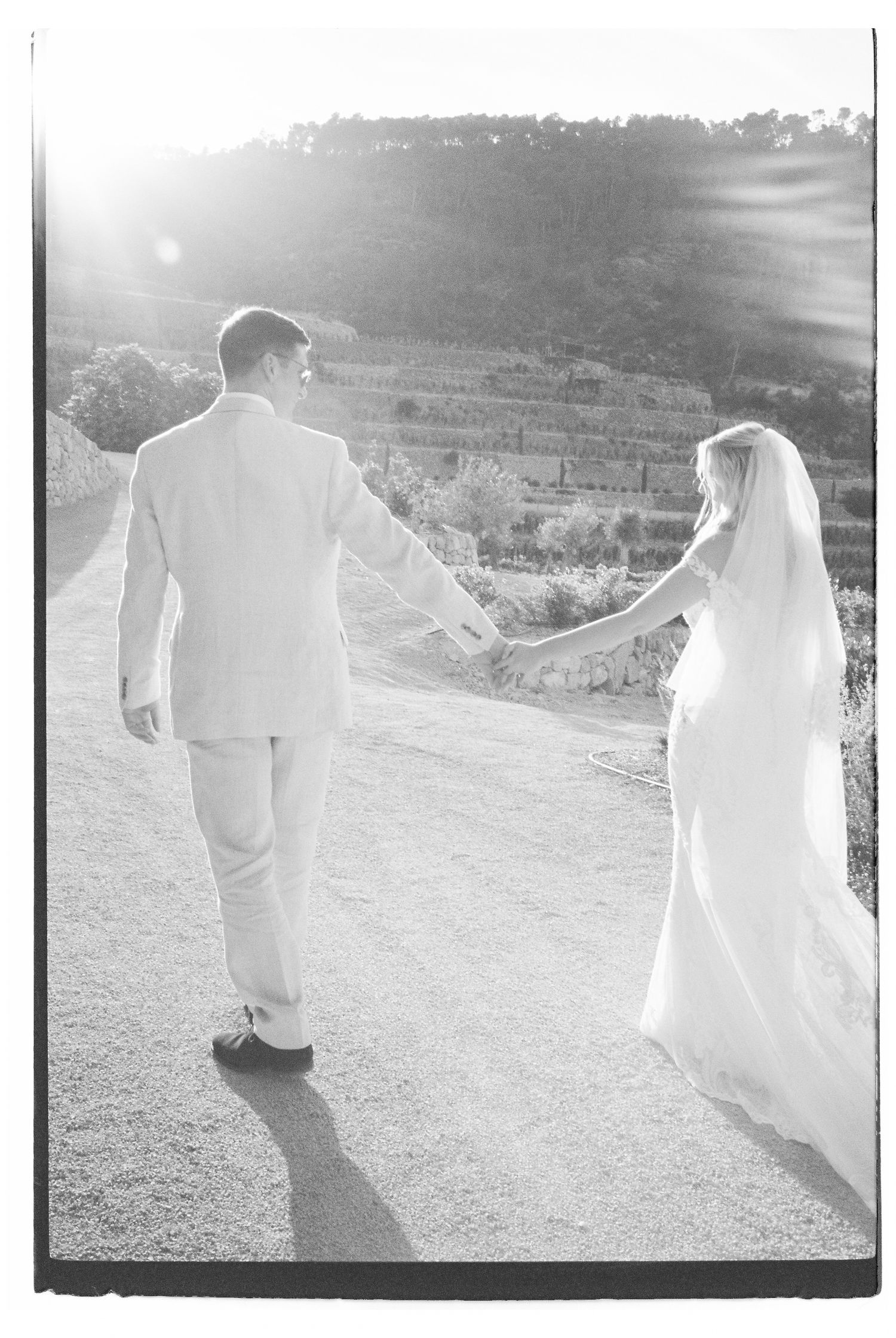 Backlit silhouette of newlyweds walking on a mountain path during sunset.