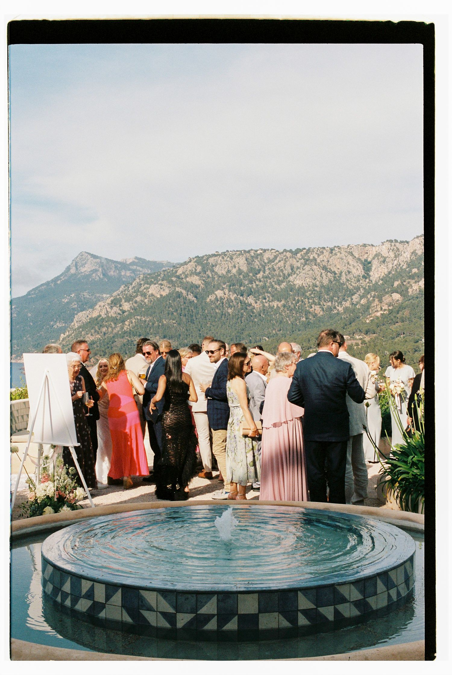 Wedding guests gathered around a circular tiled platform with mountain backdrop.