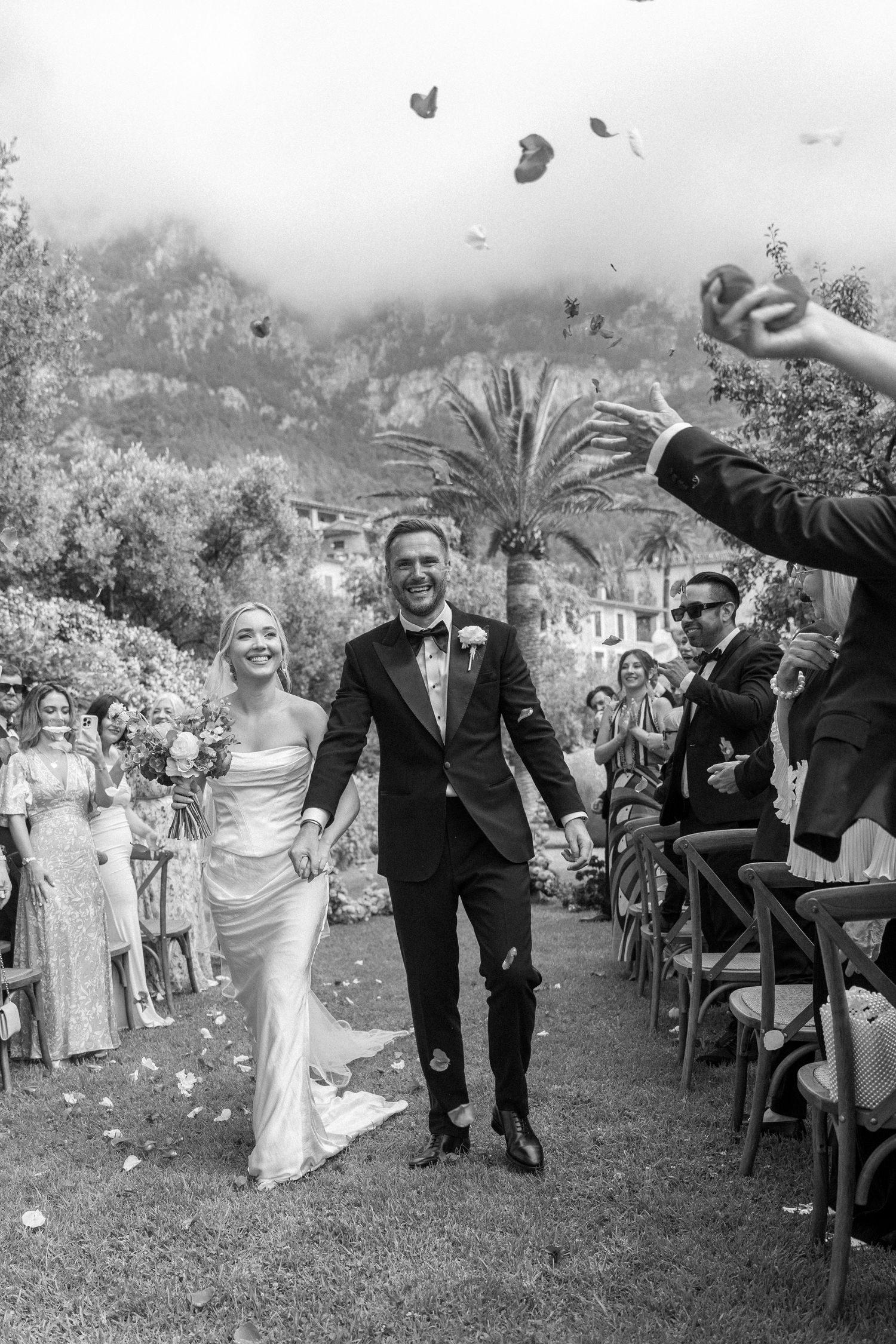 Black and white shot of newlyweds walking down aisle while guests toss confetti.