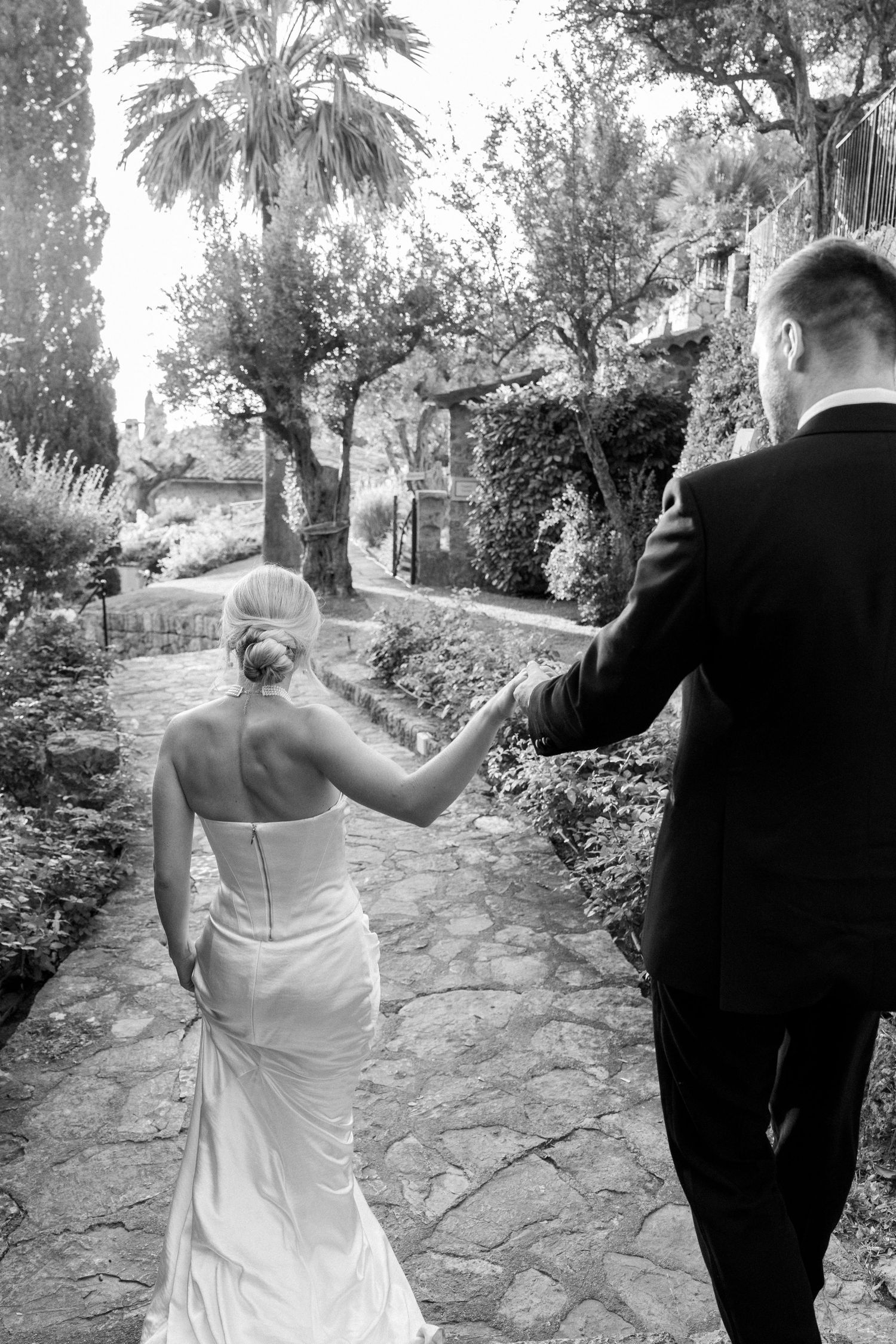 Wedding couple walking together down a stone path surrounded by greenery.