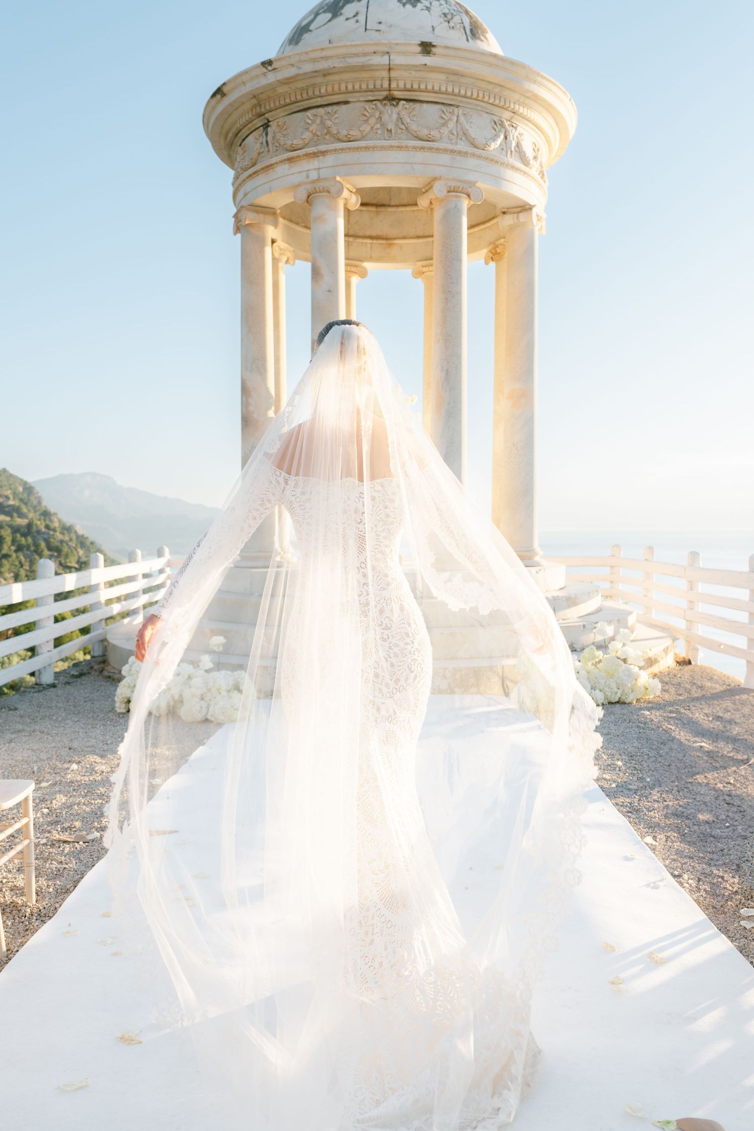 Flowing white wedding veil catches sunlight in classical domed pavilion setting.