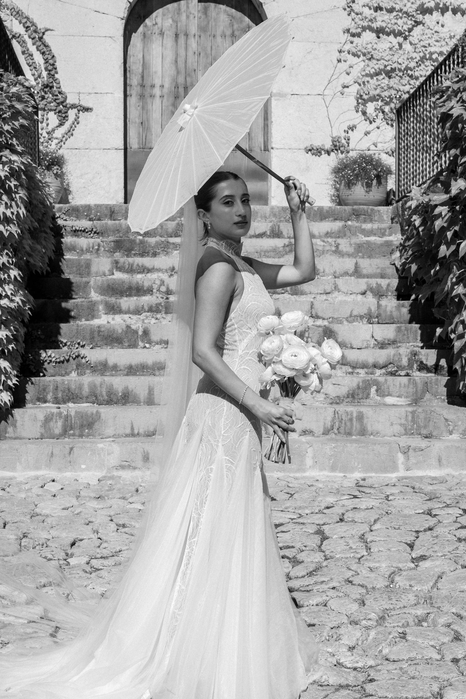 Bride with parasol poses on stone steps holding bouquet in black and white sequence.