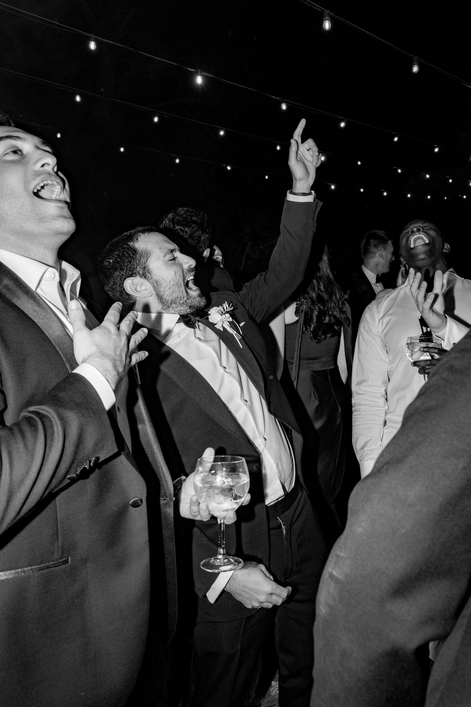 Black and white photo of groom dancing and celebrating with guests at a wedding reception.
