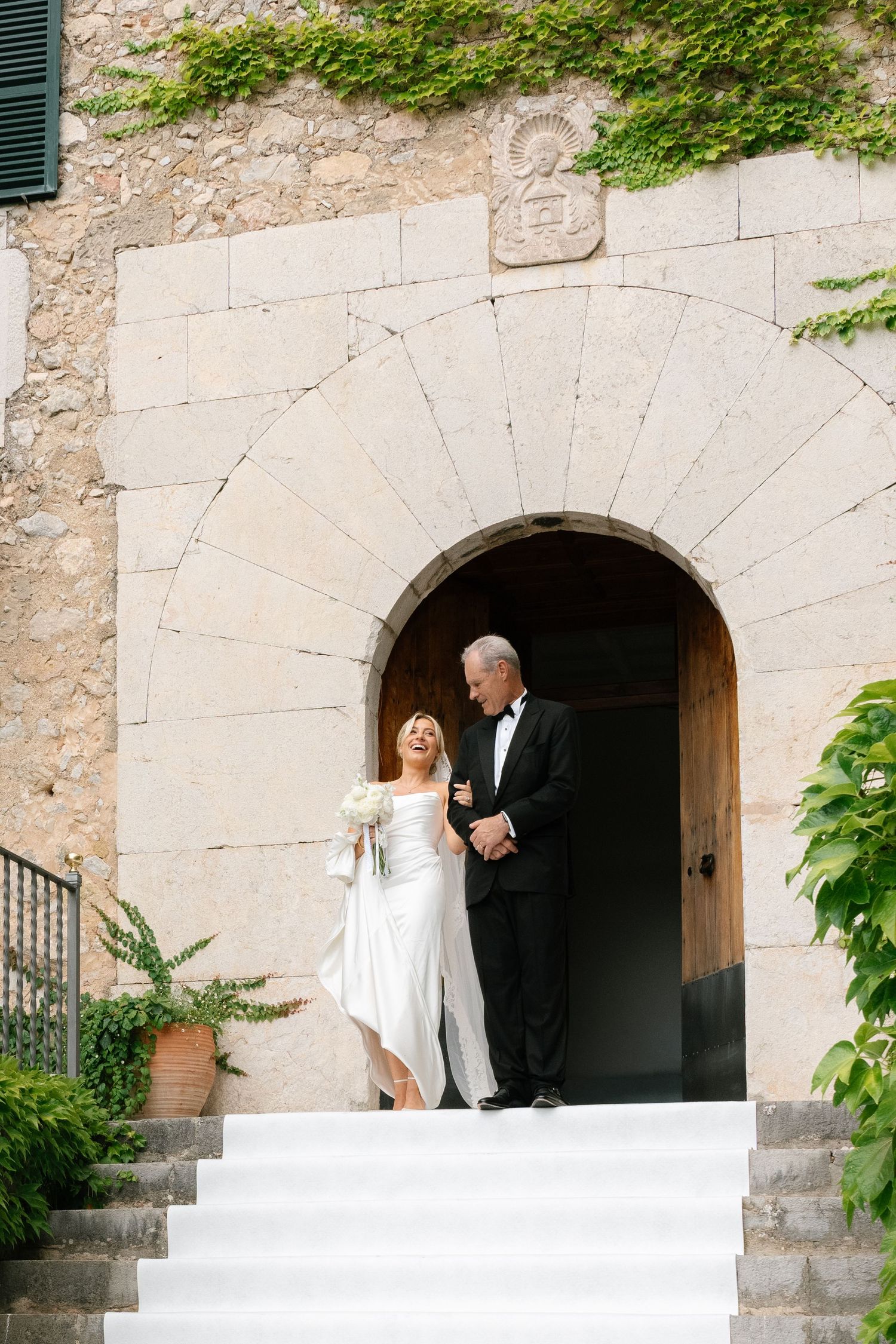 Elegant mature bride and groom in formal attire descending stone steps at a rustic European villa wedding venue.