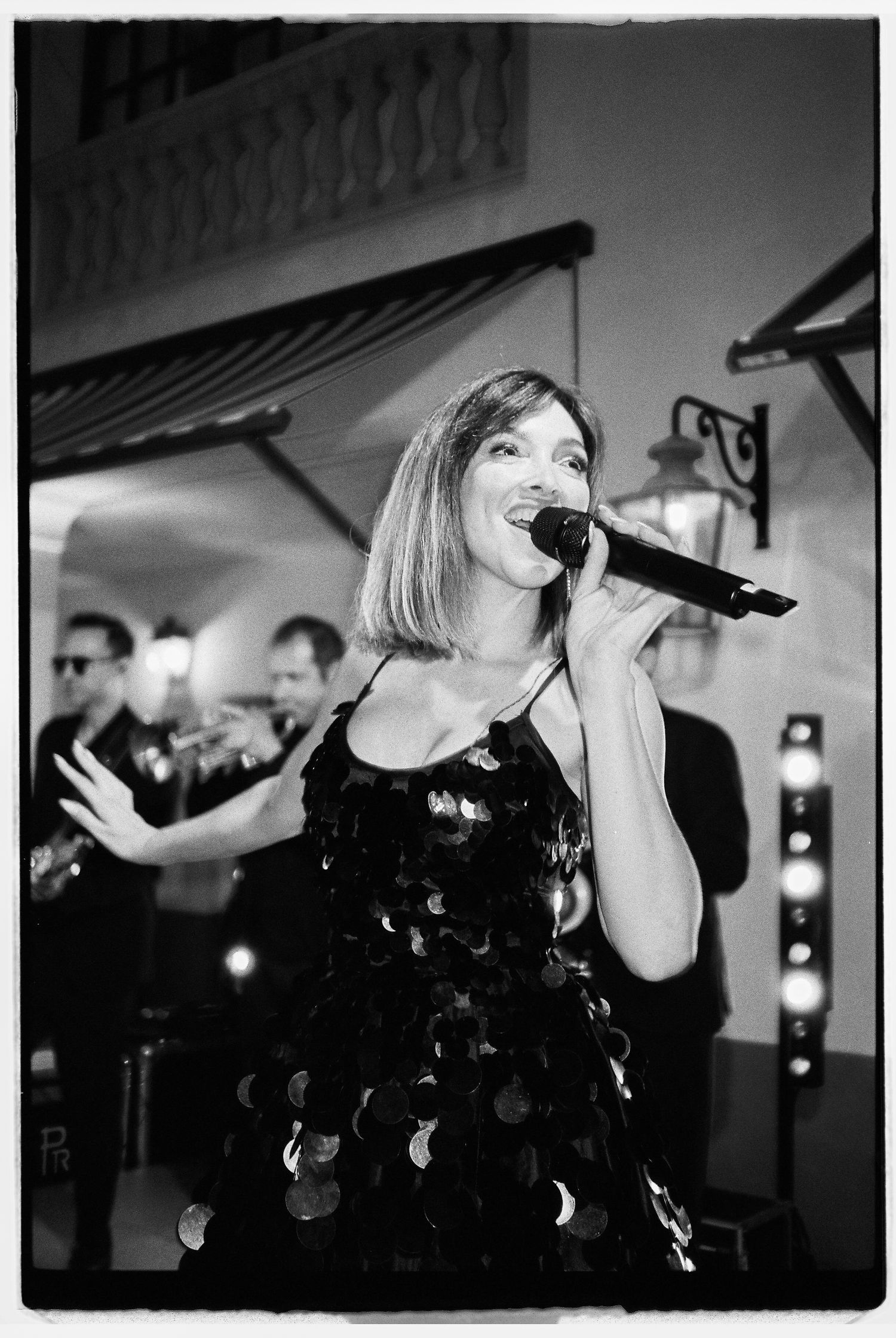 Black and white photo of a performer in a sequined dress singing on stage.
