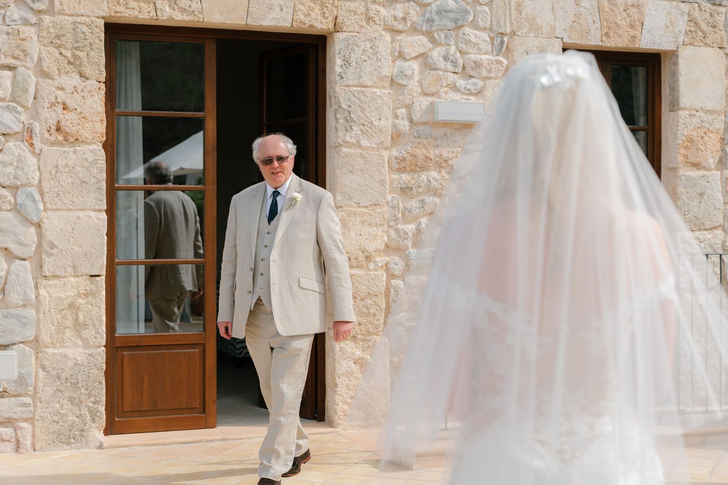 A white wedding dress with delicate lace details hangs in an outdoor stone archway.