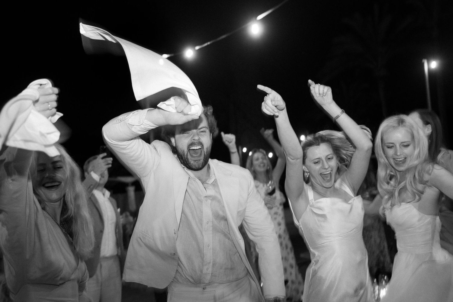 Wedding celebration with dancing guests under string lights at night.