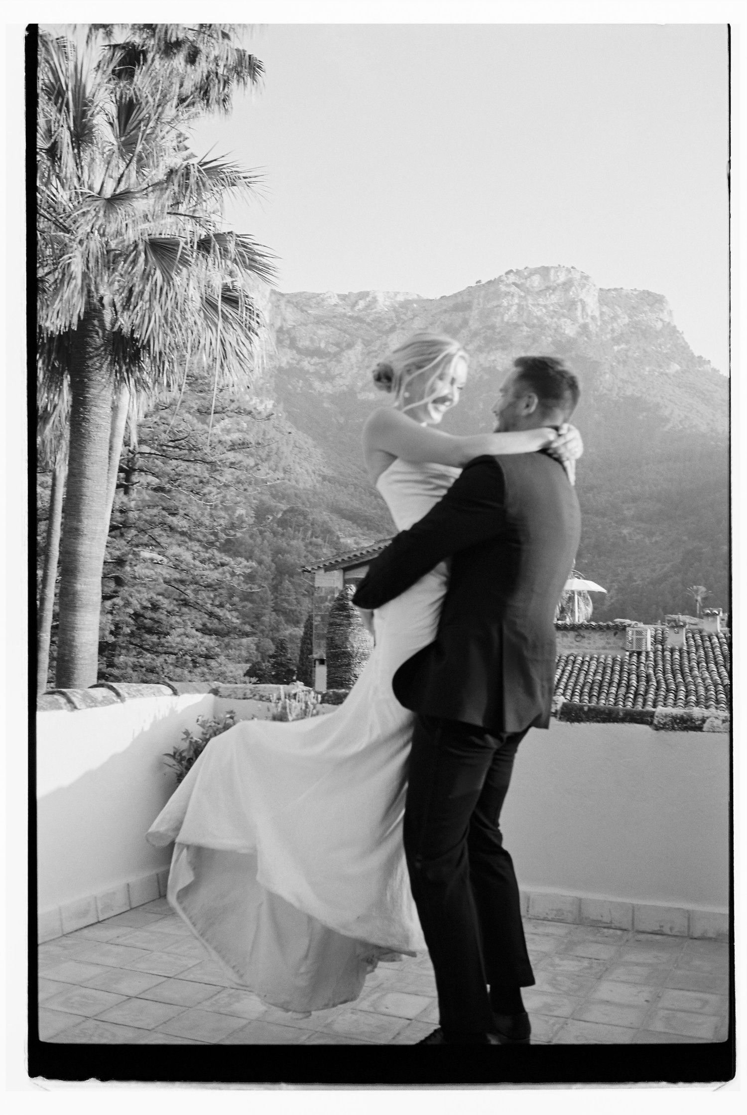 Black and white romantic dance moment on a terrace with mountain backdrop and palm trees.