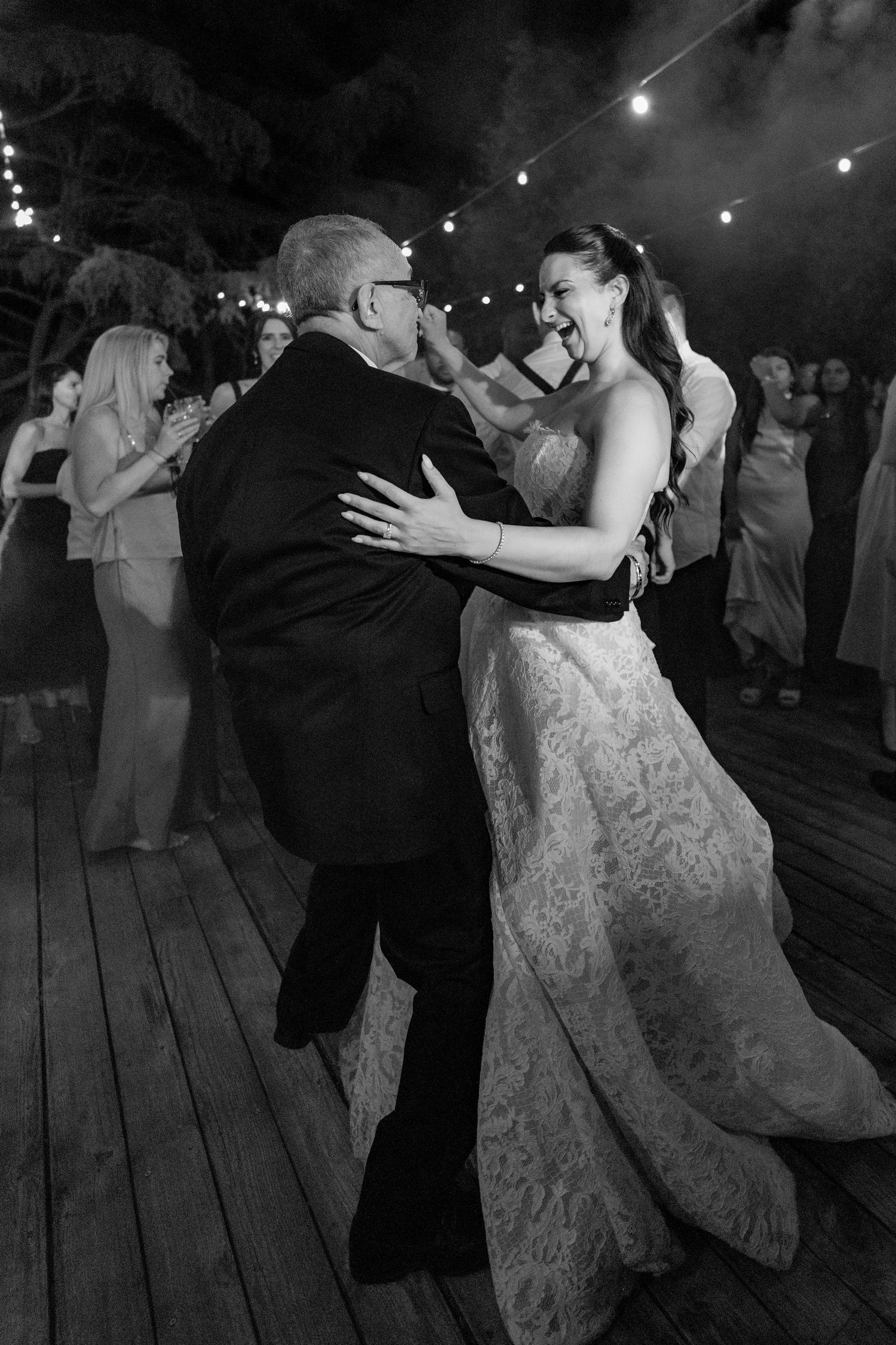 Black and white photo of a bride sharing a joyful father-daughter dance at an outdoor wedding reception.