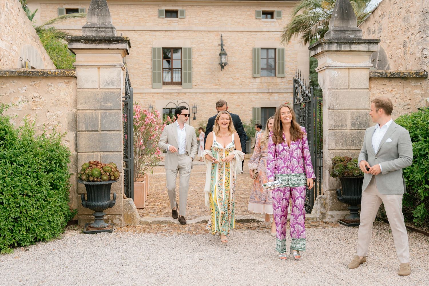 Wedding guests gather outside a rustic Mediterranean villa with stone walls.