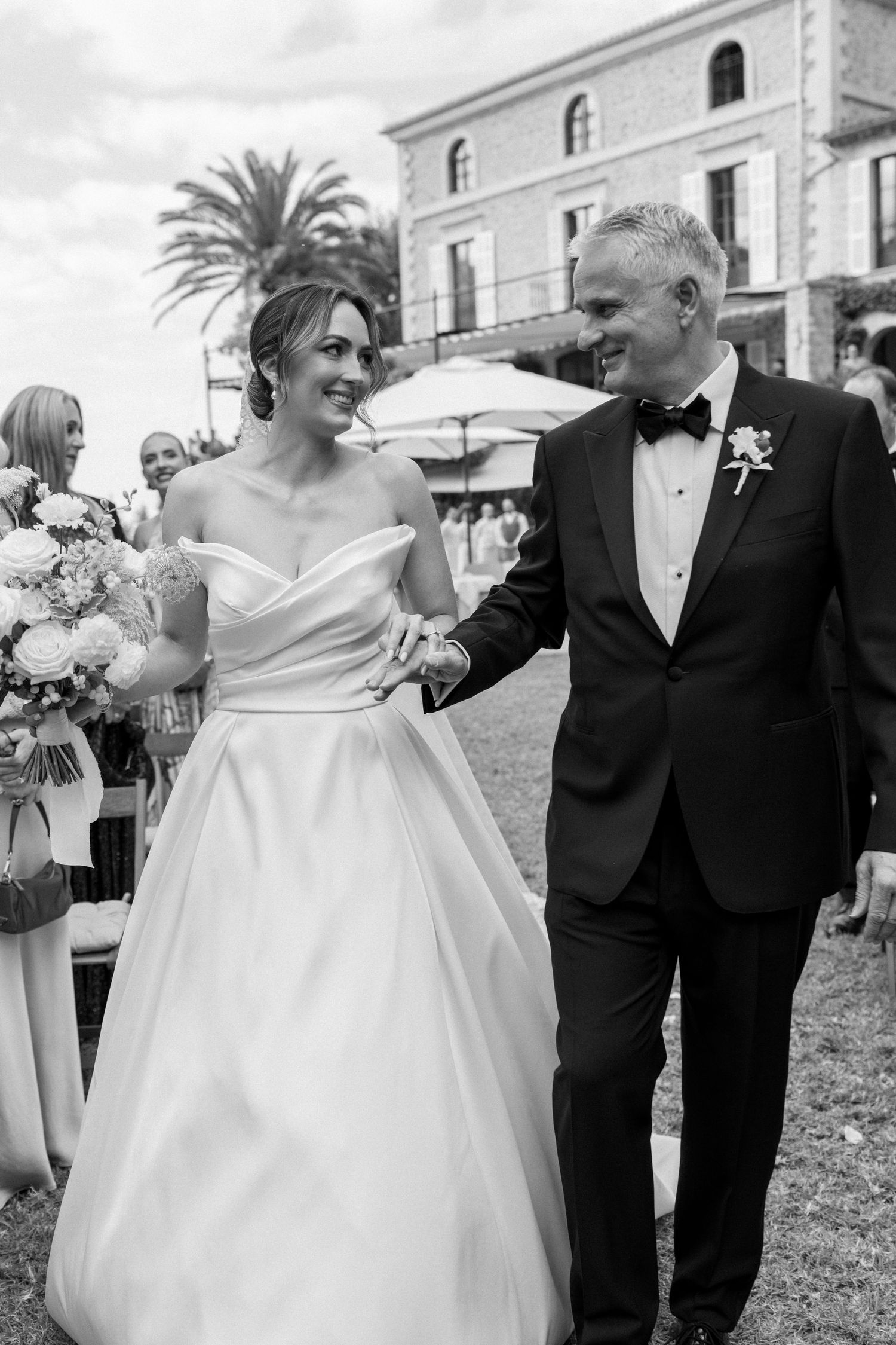 Wedding couple walking together on stone terrace with Mediterranean villa backdrop.