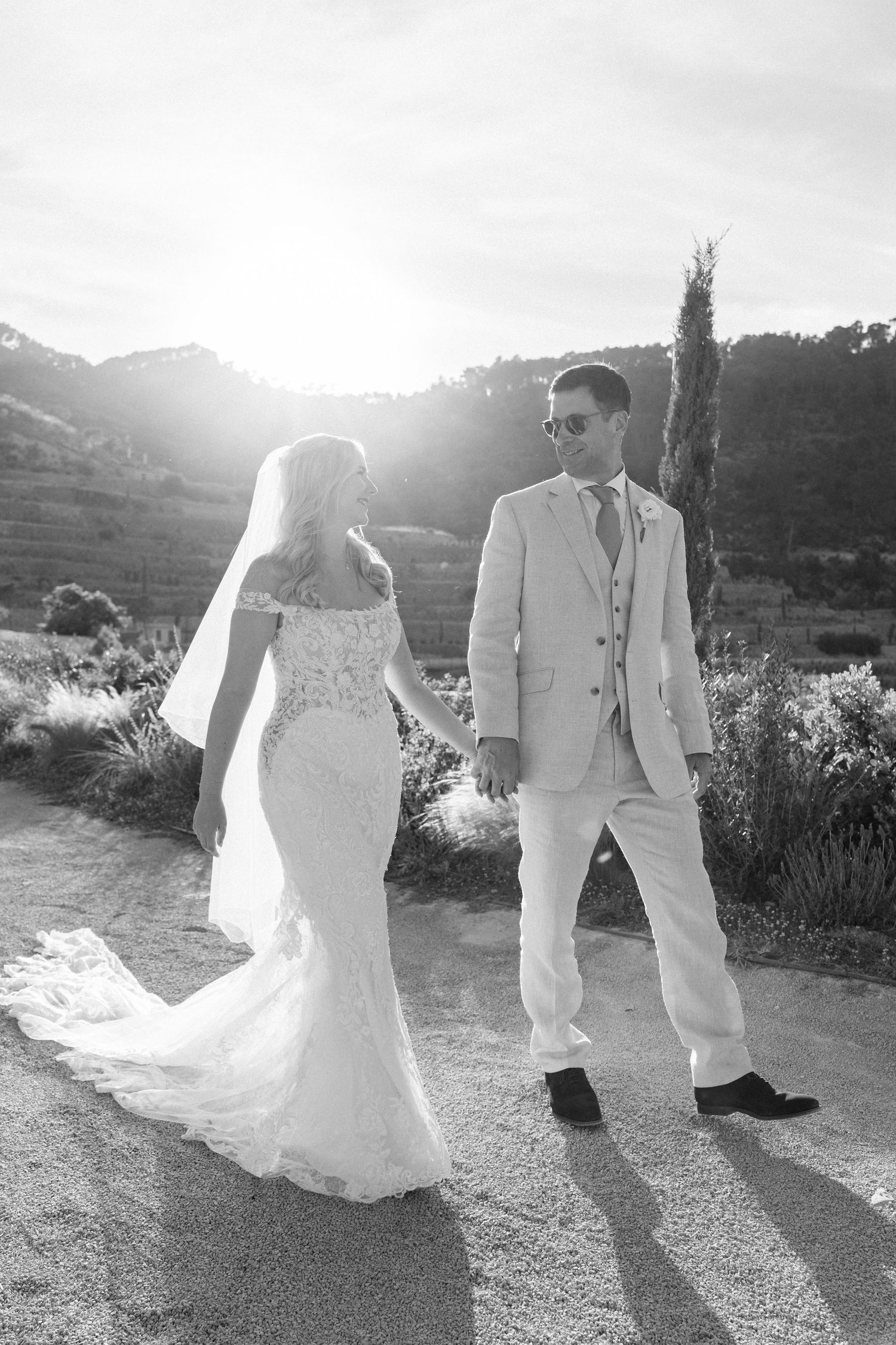 Romantic wedding couple walking together at sunset on a mountain path with long flowing dress and veil.