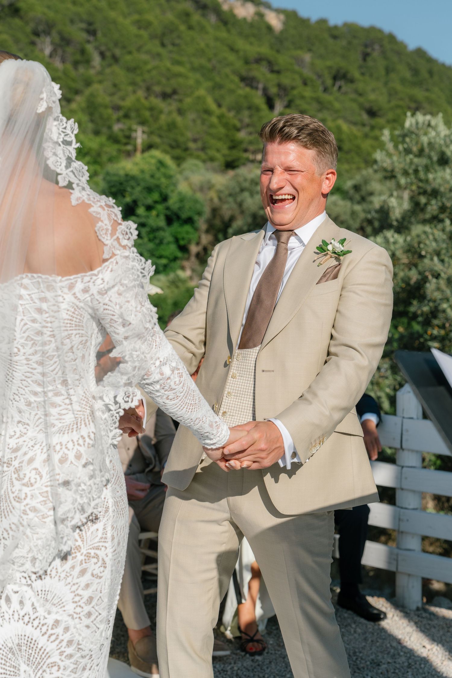 A joyful wedding moment captured outdoors with a couple laughing together in beige and white attire.