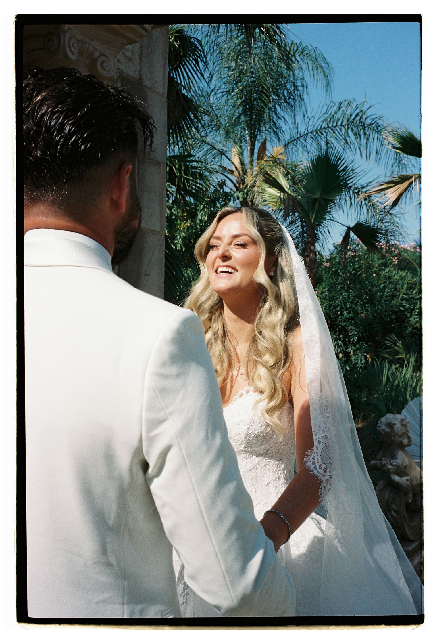Newlyweds share joyful expressions against a tropical palm tree backdrop.