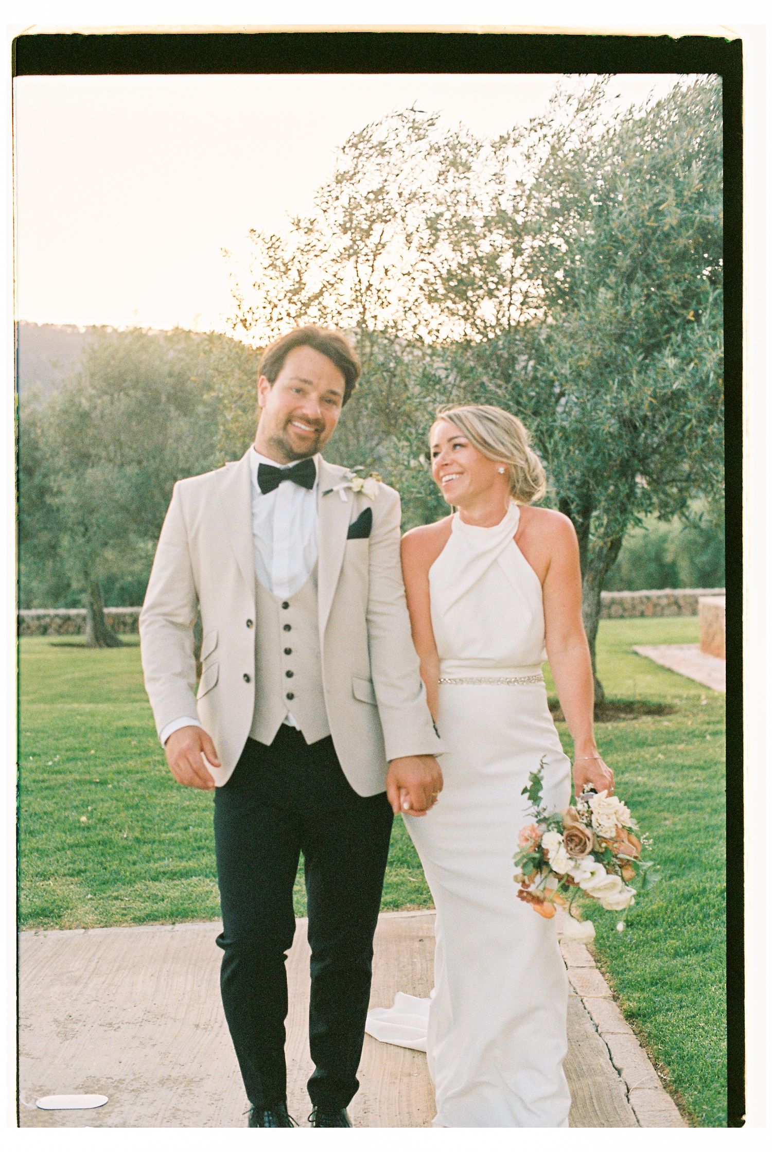 A couple walking and laughing together on a garden path at sunset.