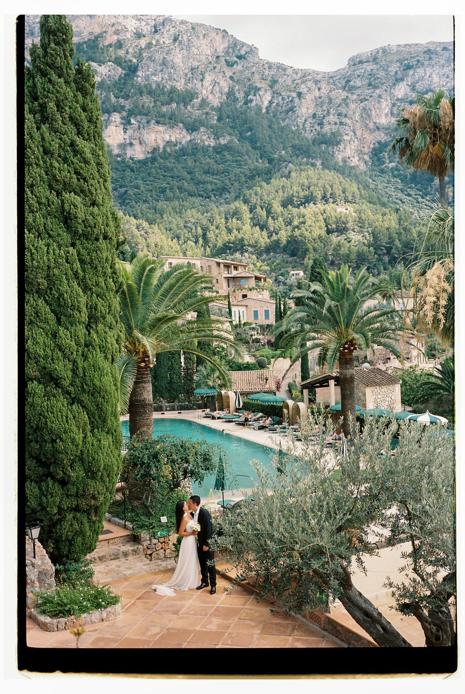 Wedding couple poses by luxury pool with mountain views at Mediterranean resort.