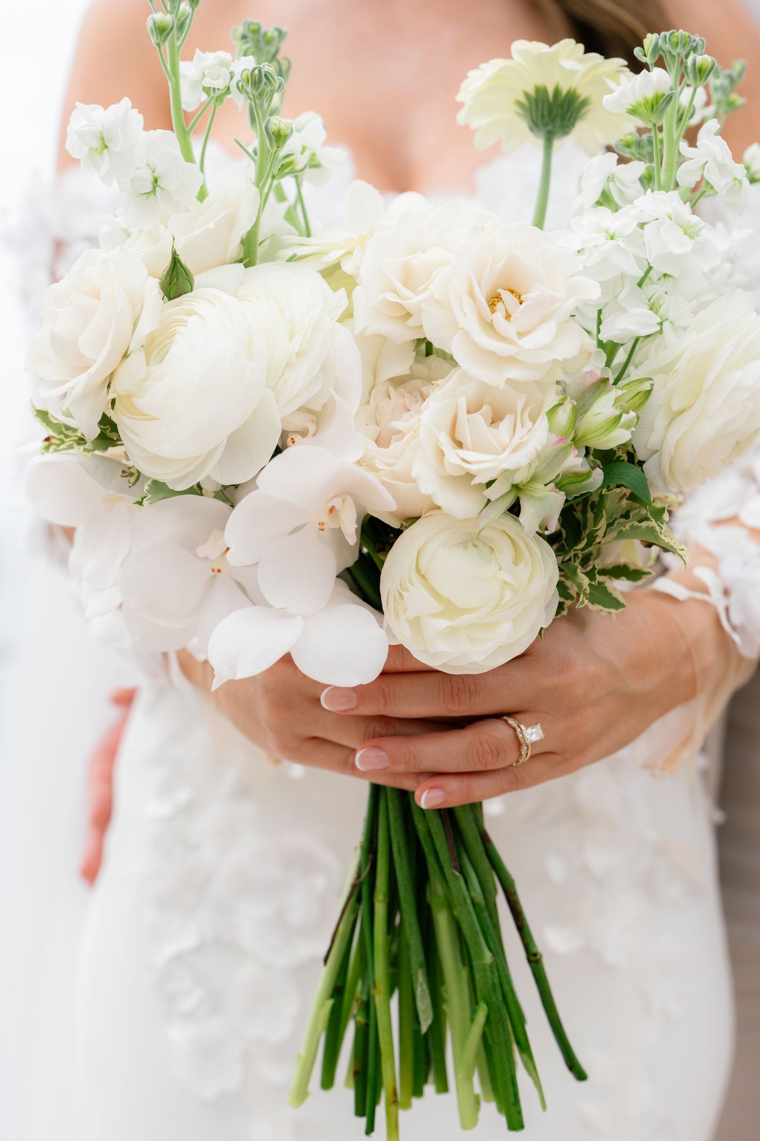 Elegant white rose and greenery wedding bouquet held against a light background.