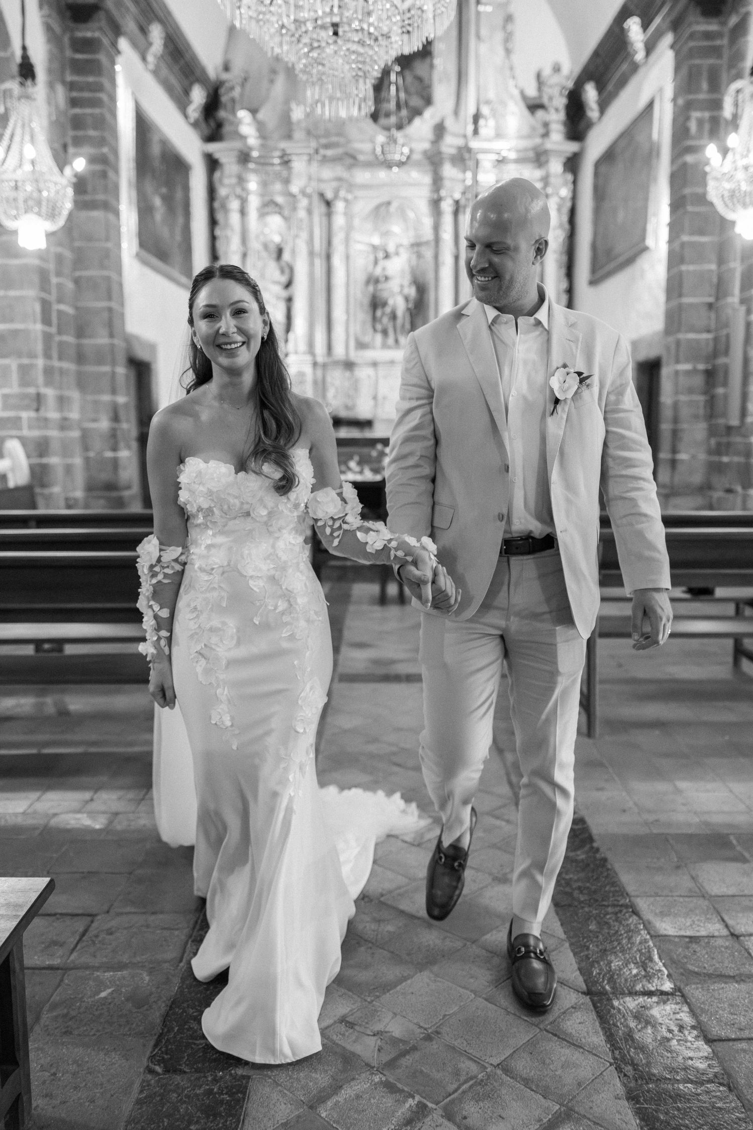 Wedding couple walking through an elegant church interior with crystal chandeliers.