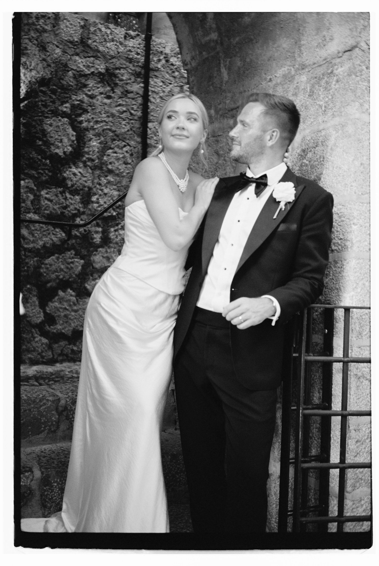 Elegant black and white wedding portrait against a stone wall backdrop.