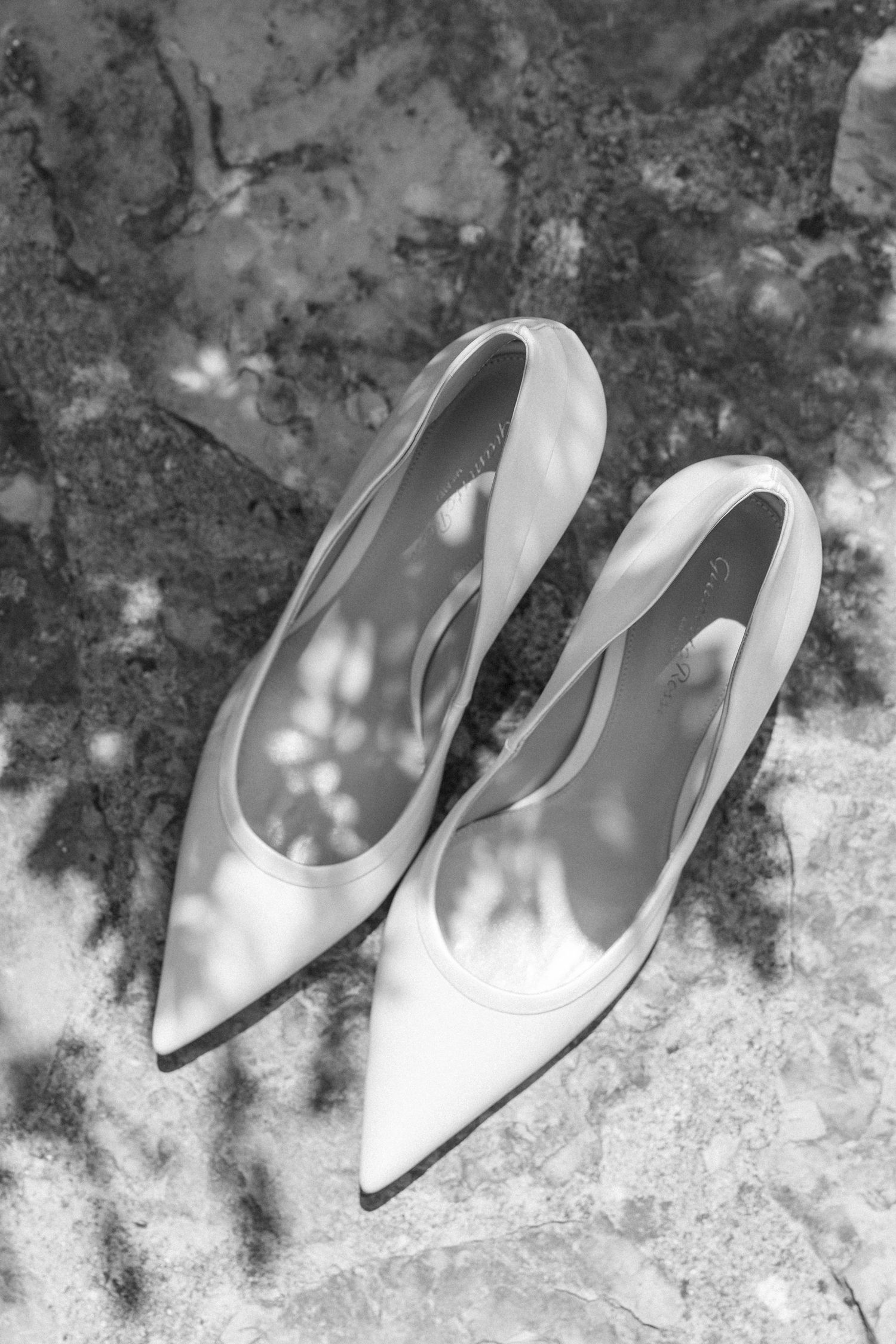 Elegant white bridal shoes arranged on a textured stone surface in natural lighting.