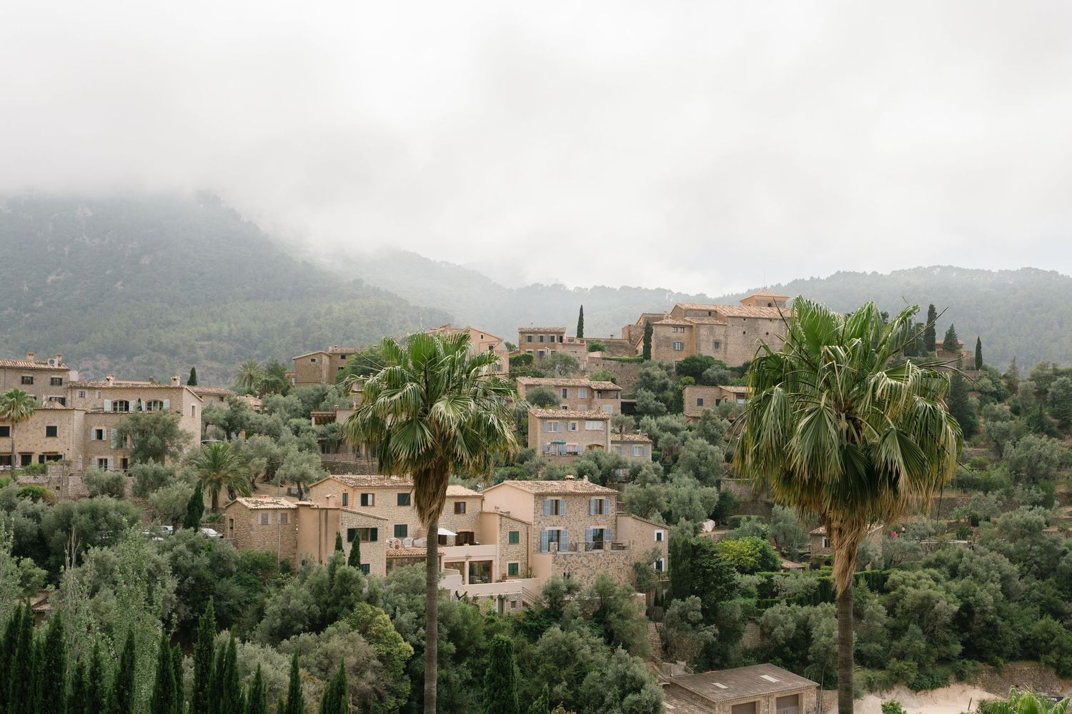 Panoramic view of Mediterranean hillside village with stone buildings and palm trees.
