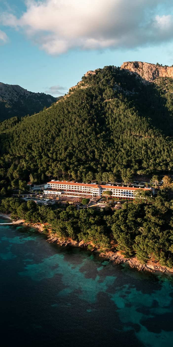Aerial view of a luxury beachfront hotel Four Seasons nestled among lush green pine forests beside turquoise Mediterranean waters.