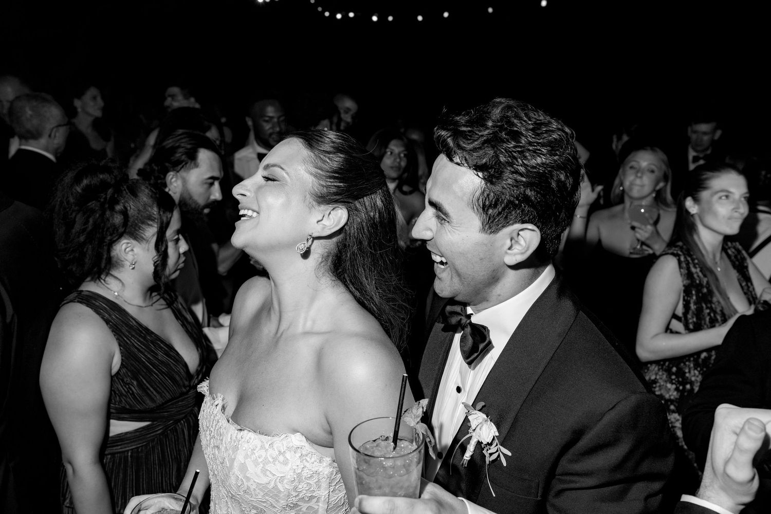 Black and white photo of a joyful bride and groom laughing together at their wedding reception.