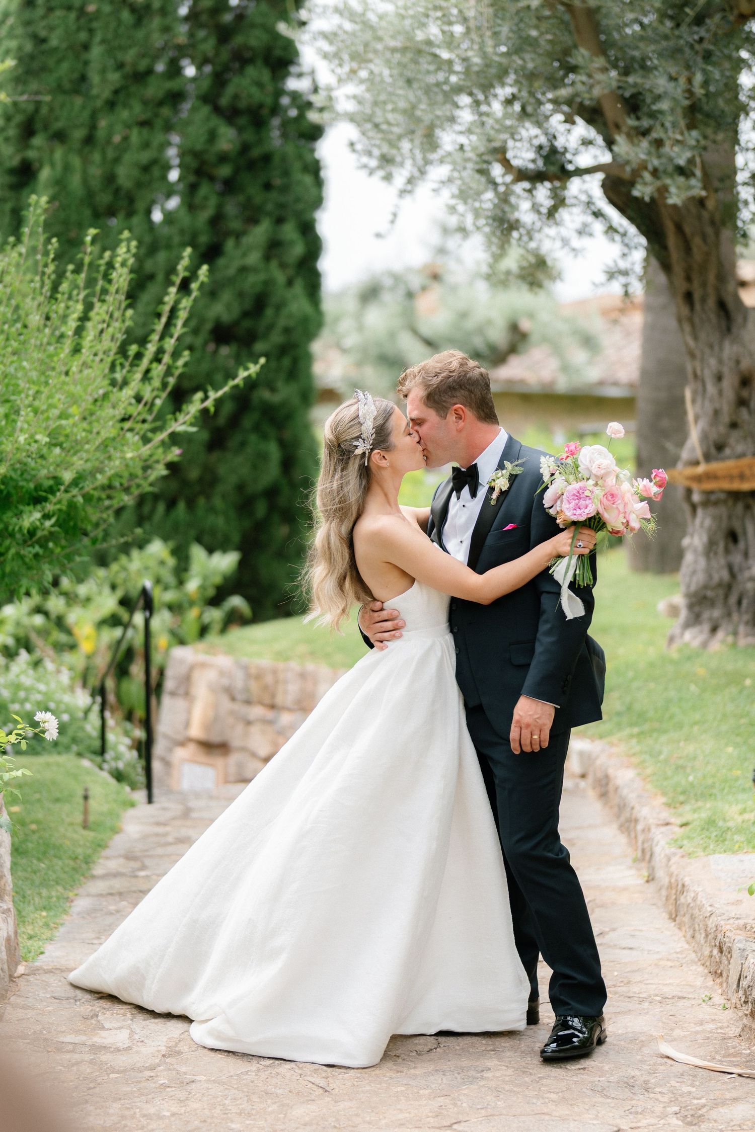 Romantic wedding couple embrace on a garden path surrounded by lush greenery.