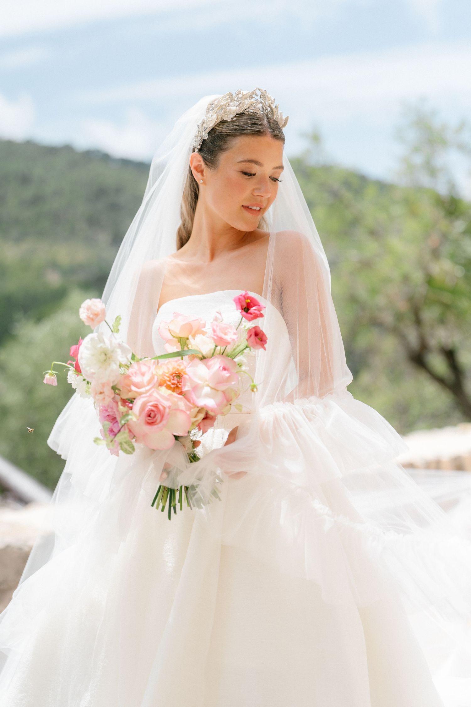 Bride holding beautiful pink and coral rose bouquet against mountain landscape.