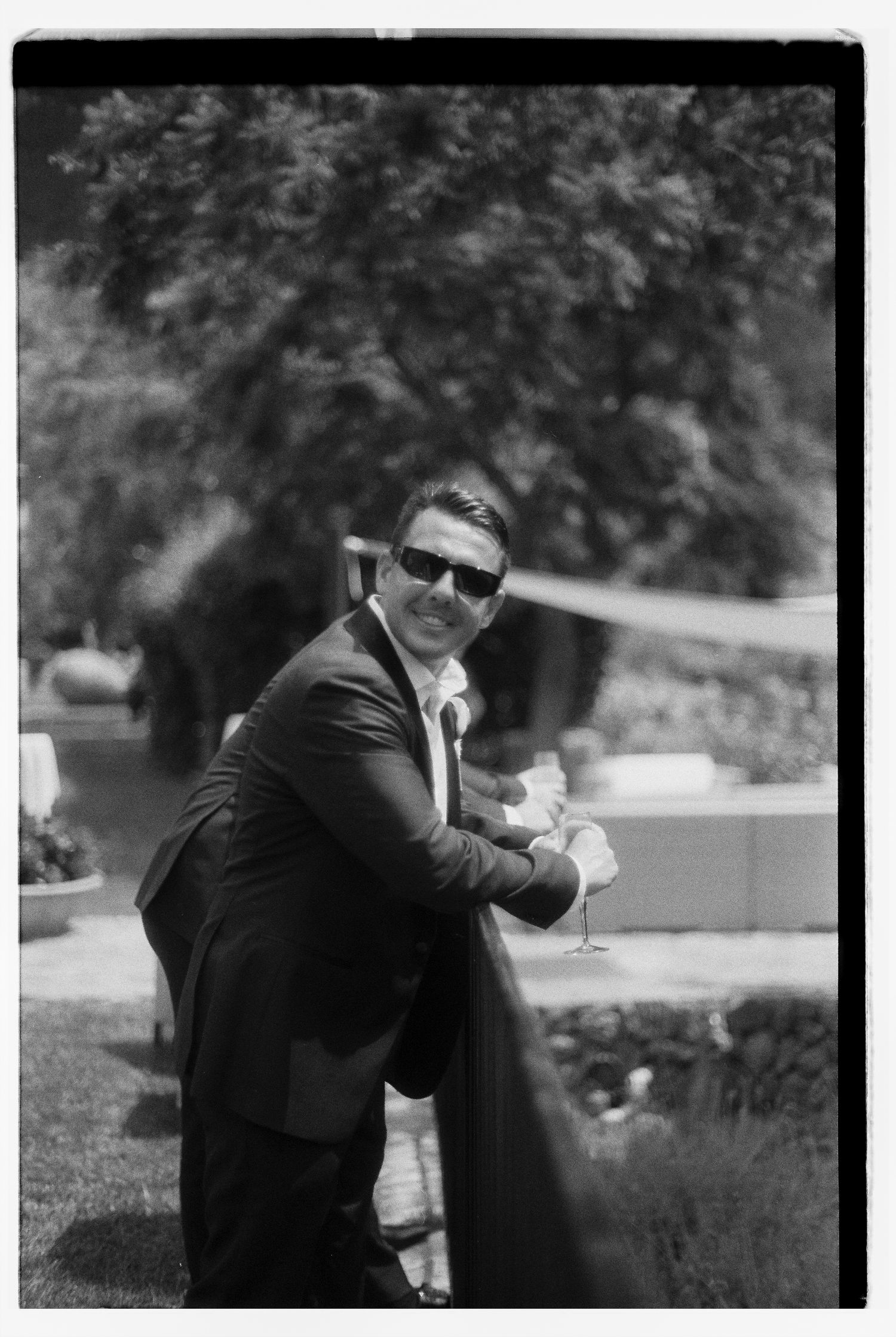 Black and white portrait of guest in suit holding champagne at outdoor event.