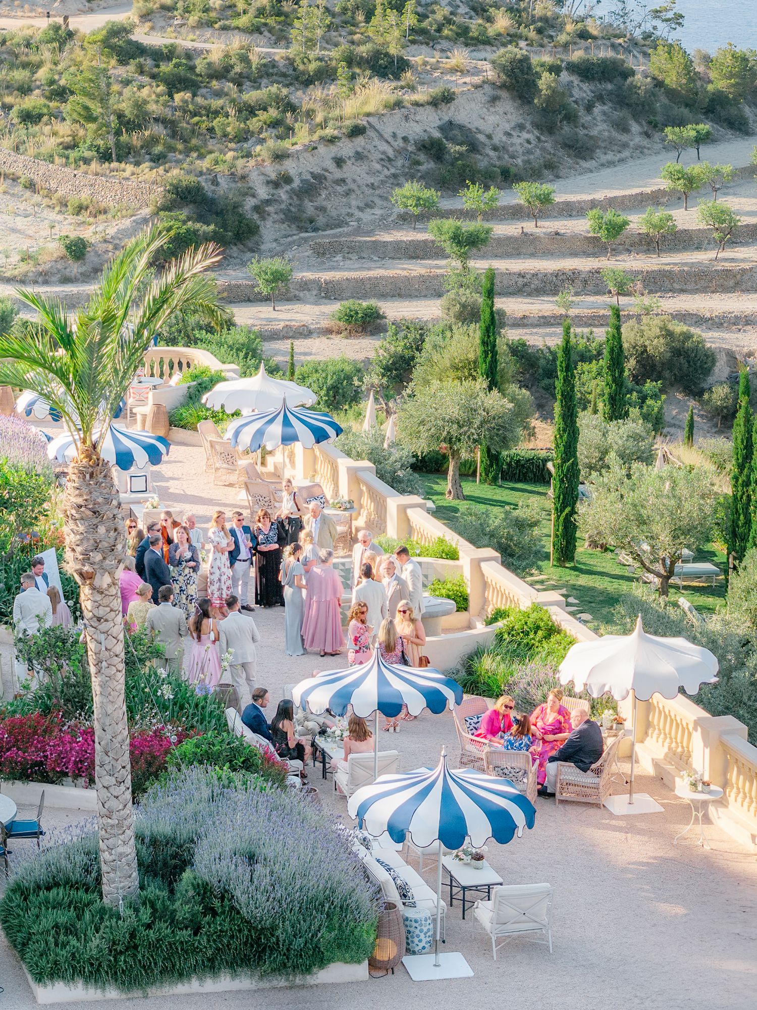 Mediterranean garden terrace with striped umbrellas and guests enjoying an outdoor wedding reception.